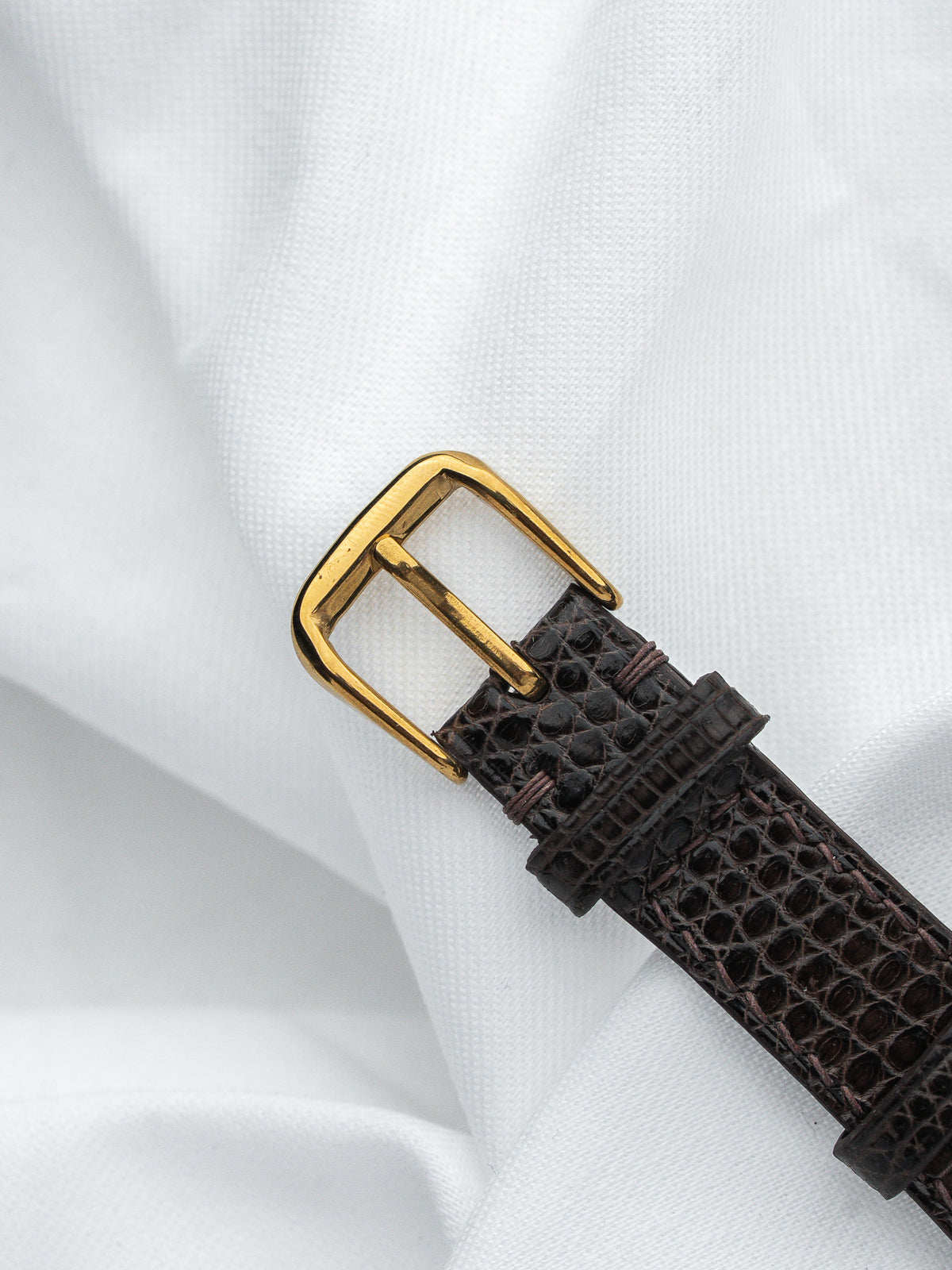 Vintage watch strap with brown alligator texture and gold buckle on white fabric