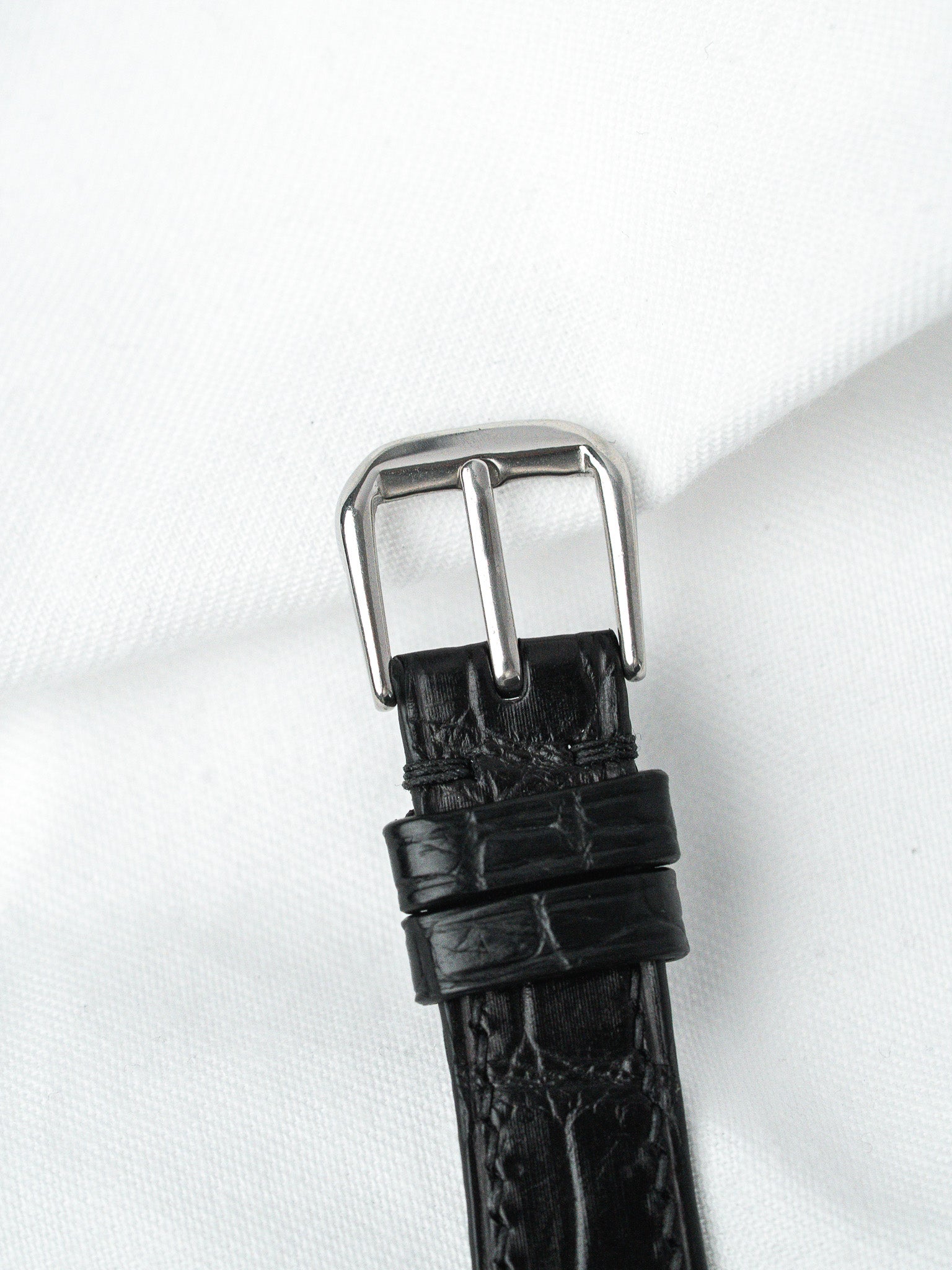 Black alligator leather watch strap with polished steel buckle on white fabric