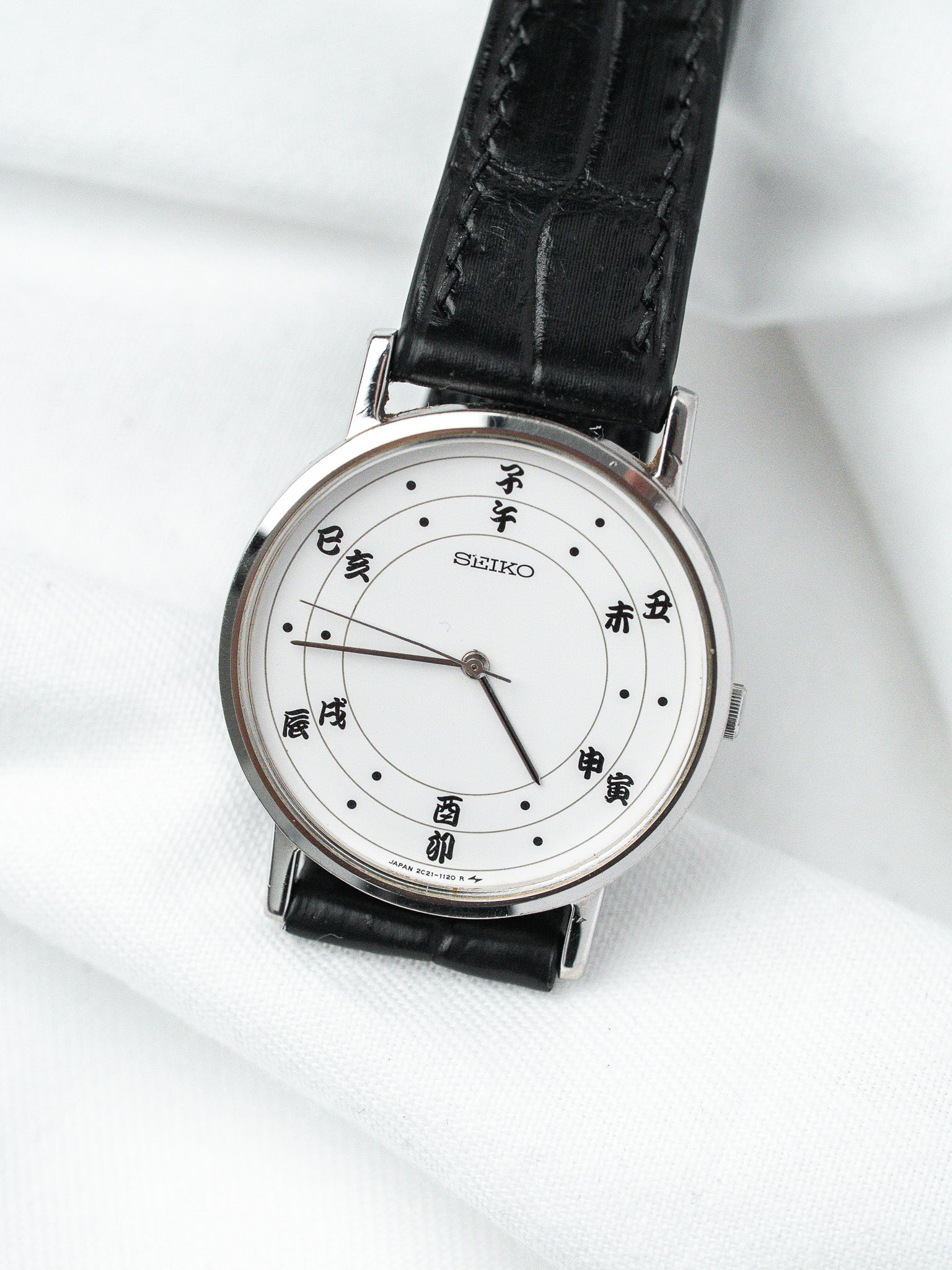 Seiko vintage watch with white dial, Japanese characters, black leather strap on white fabric