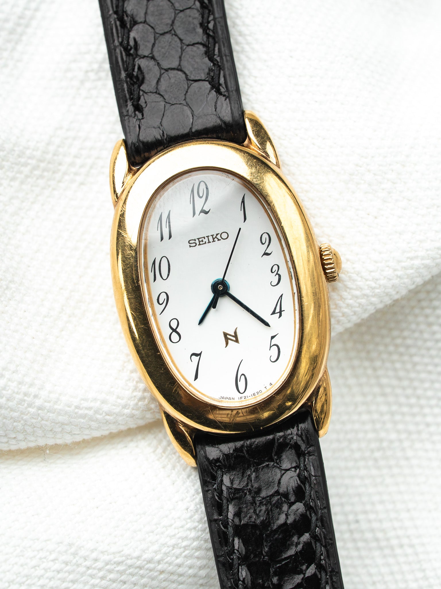 Seiko vintage watch with gold case, white dial, black alligator strap on white fabric