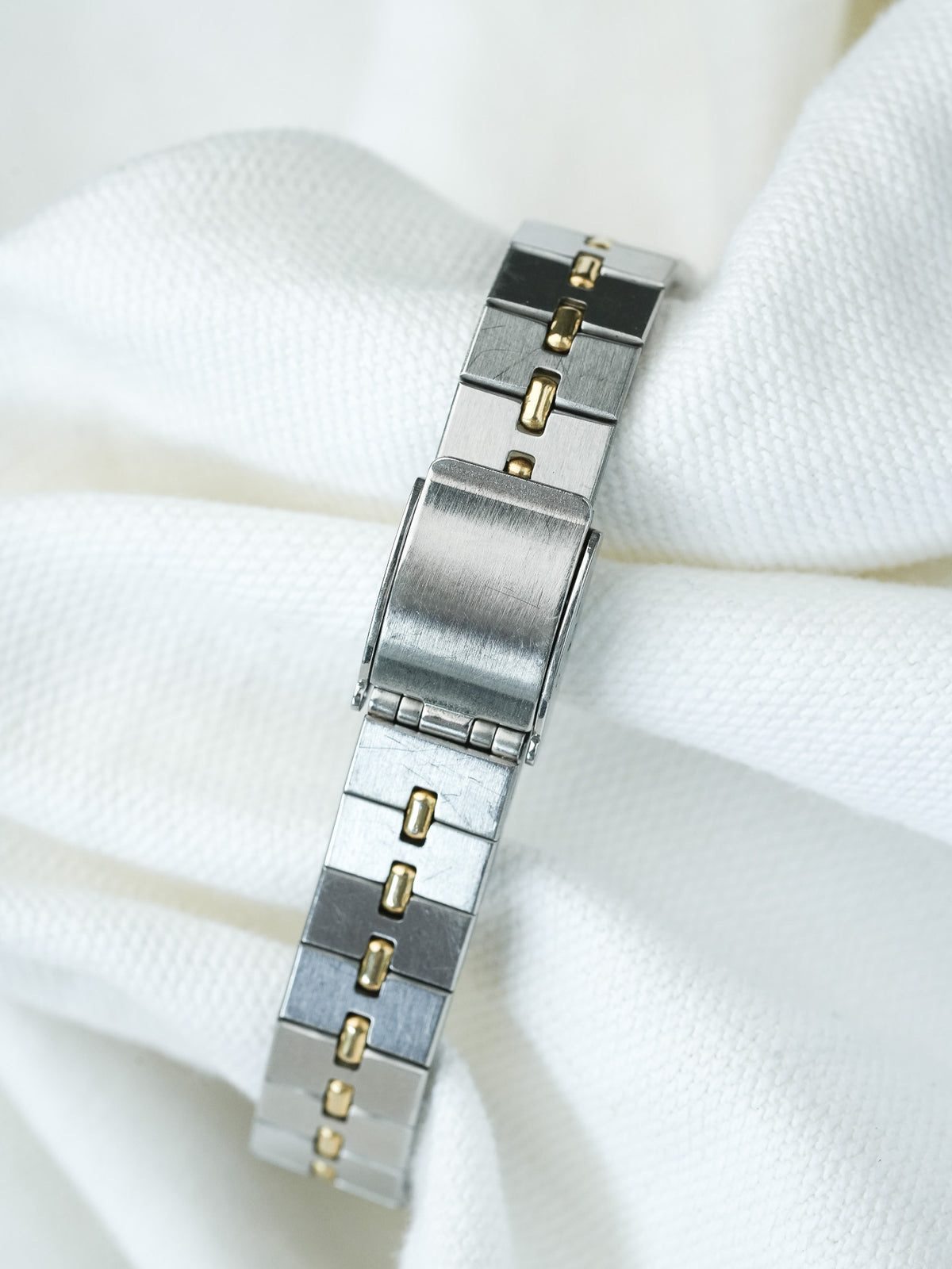 Vintage Omega bracelet in two-tone steel and gold, resting on white fabric