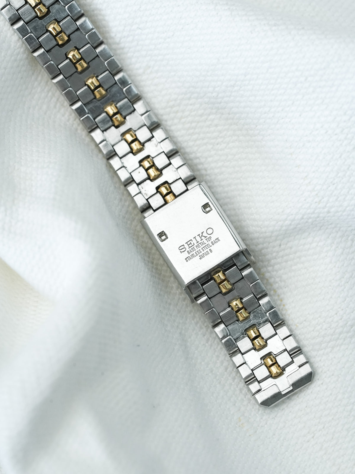 Seiko vintage watch bracelet, two-tone steel and gold links, white fabric background