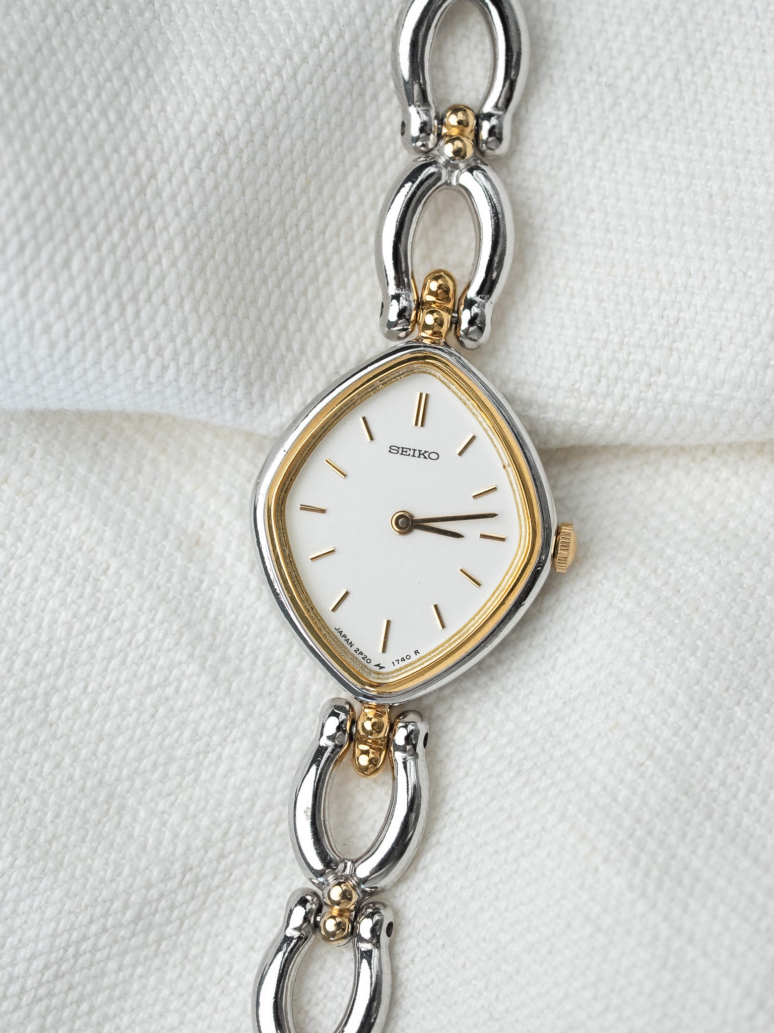 Seiko vintage watch with white dial, gold accents, and two-tone bracelet on textured white background