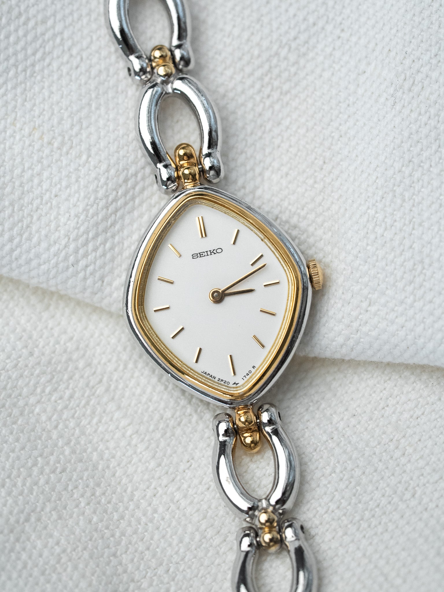 Seiko vintage watch with white dial, gold accents, and two-tone bracelet on textured white background