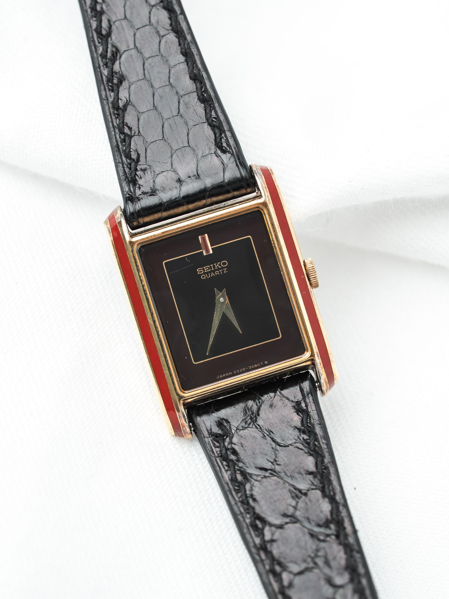 Seiko Quartz vintage watch with gold case, black dial, red accents, and black alligator strap