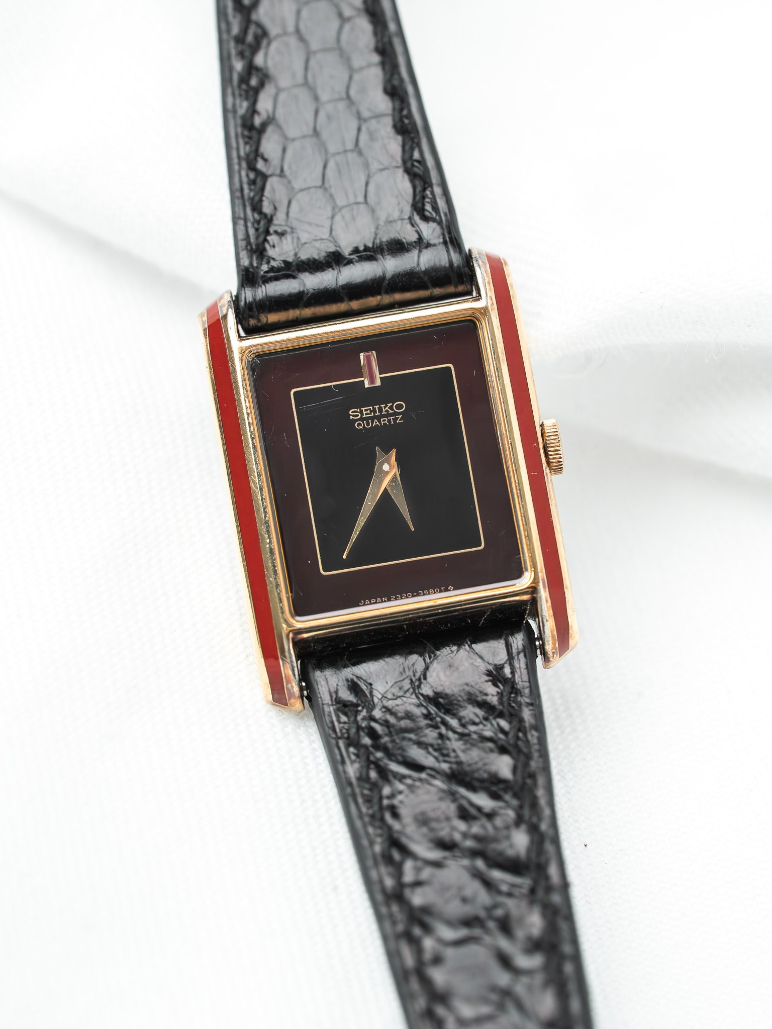 Seiko Quartz vintage watch with gold case, black dial, red accents, and black textured strap