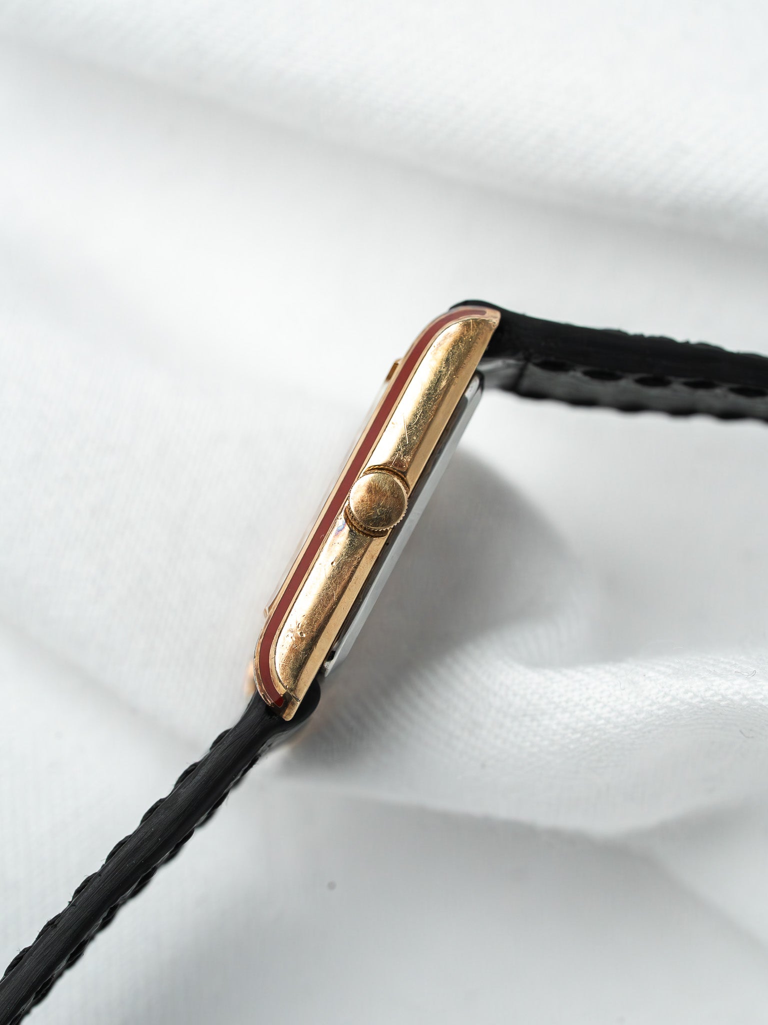 Vintage Cartier watch with gold case, red accent, black leather strap on white fabric