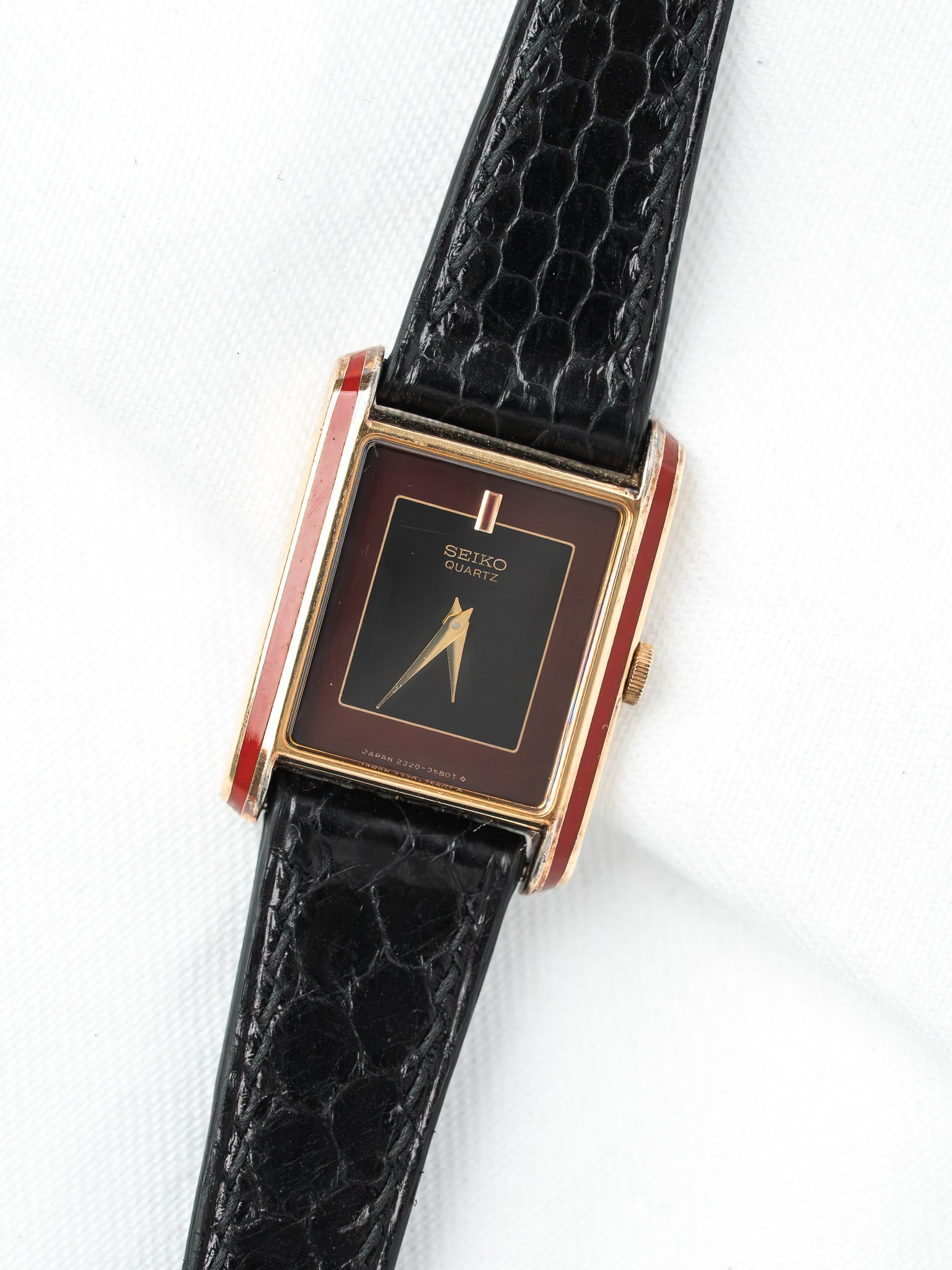 Seiko Quartz vintage watch with gold case, black dial, red accents, and black textured strap