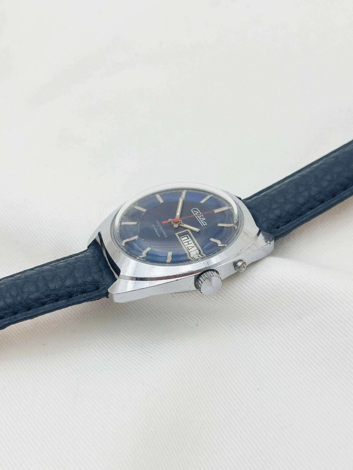 Vintage Vostok watch with blue dial, silver case, and dark leather strap on white background