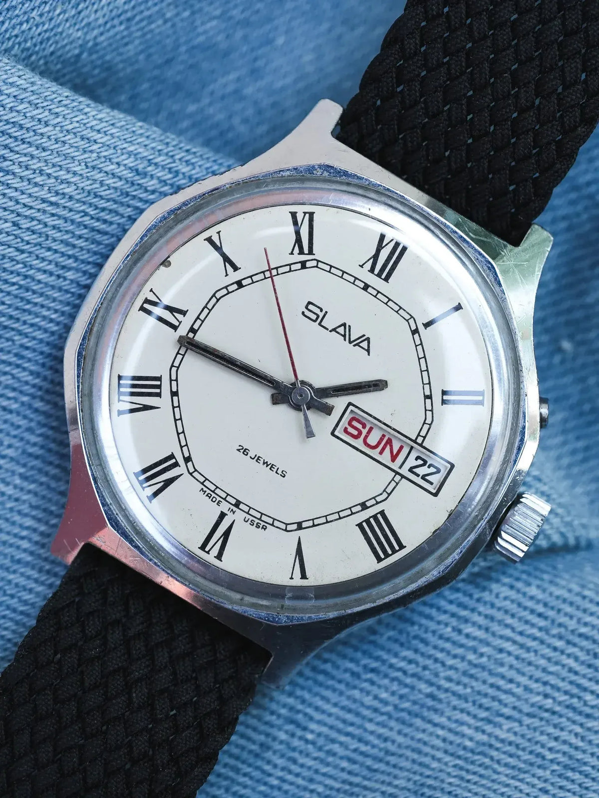 Vintage Slava watch with white dial, Roman numerals, black fabric strap, worn on denim
