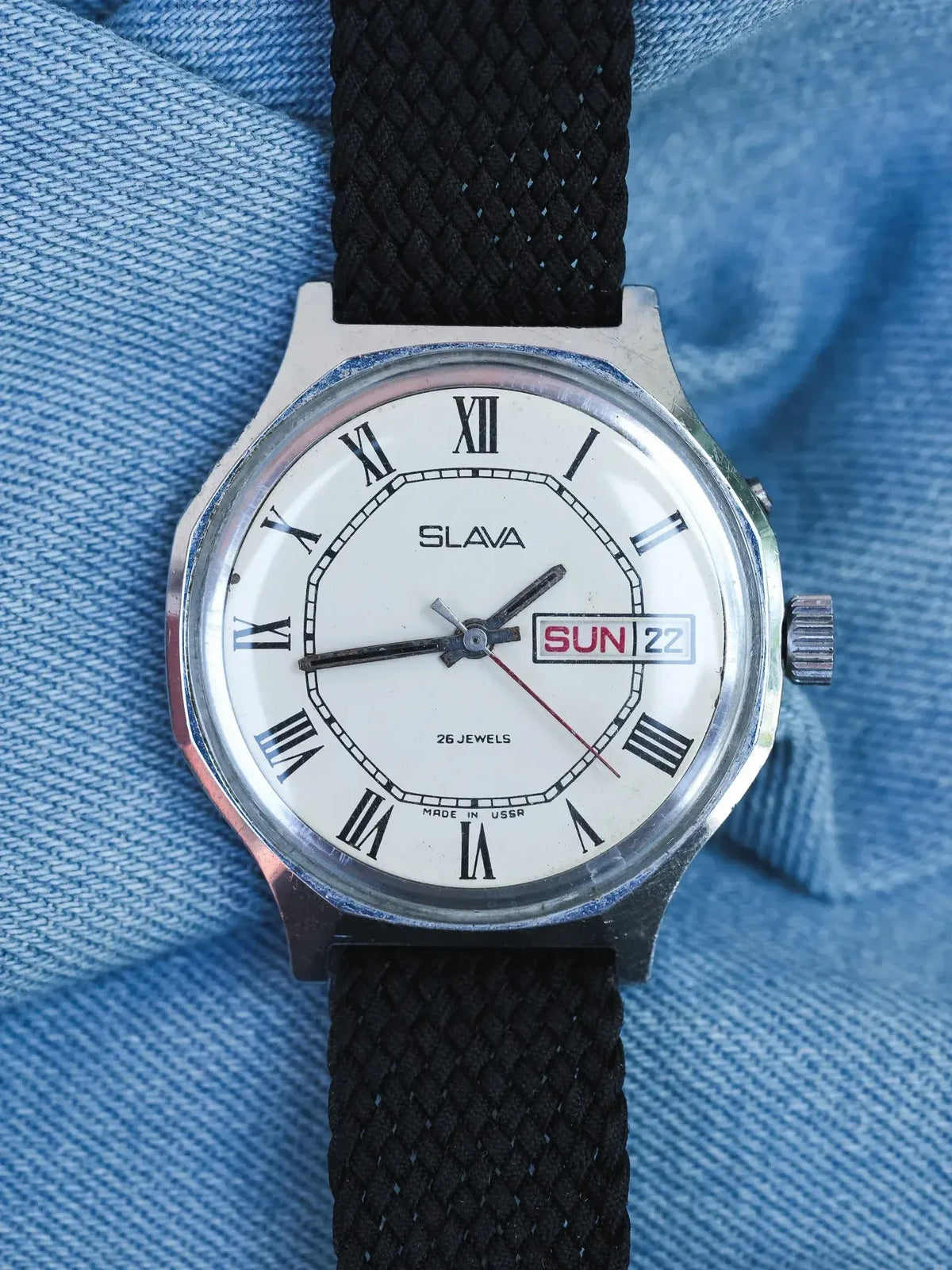 Vintage Slava watch with white dial, Roman numerals, black fabric strap on denim