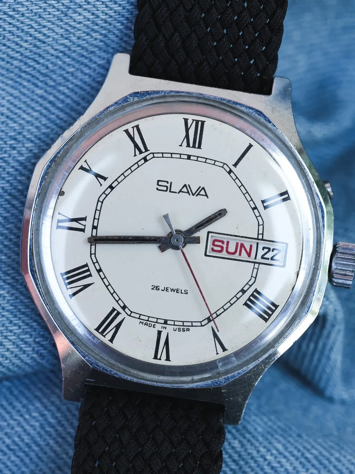 Slava vintage watch with white dial, Roman numerals, black fabric strap on denim