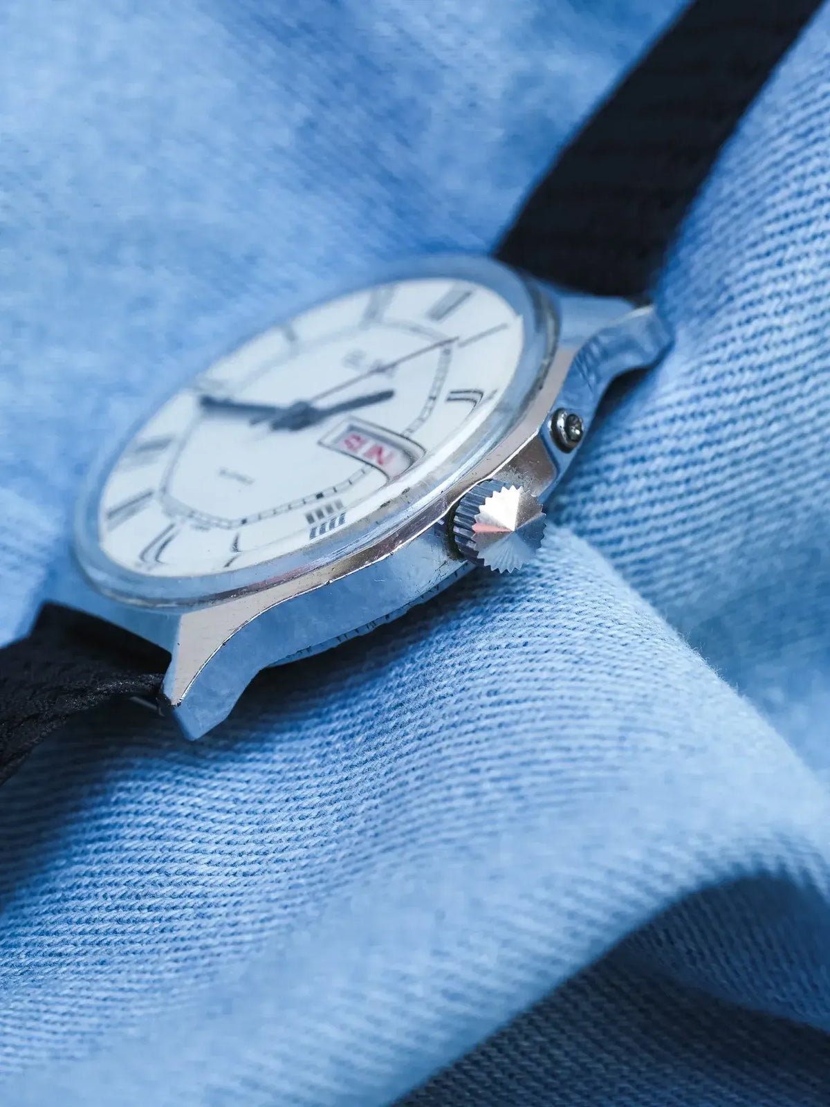 Vintage Omega watch with white dial, black strap, on blue fabric background