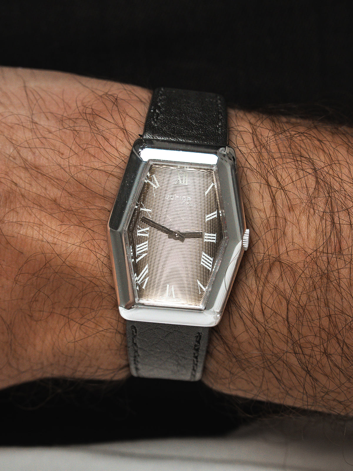 Montre vintage au boîtier hexagonal argenté, cadran texturé et bracelet cuir noir au poignet