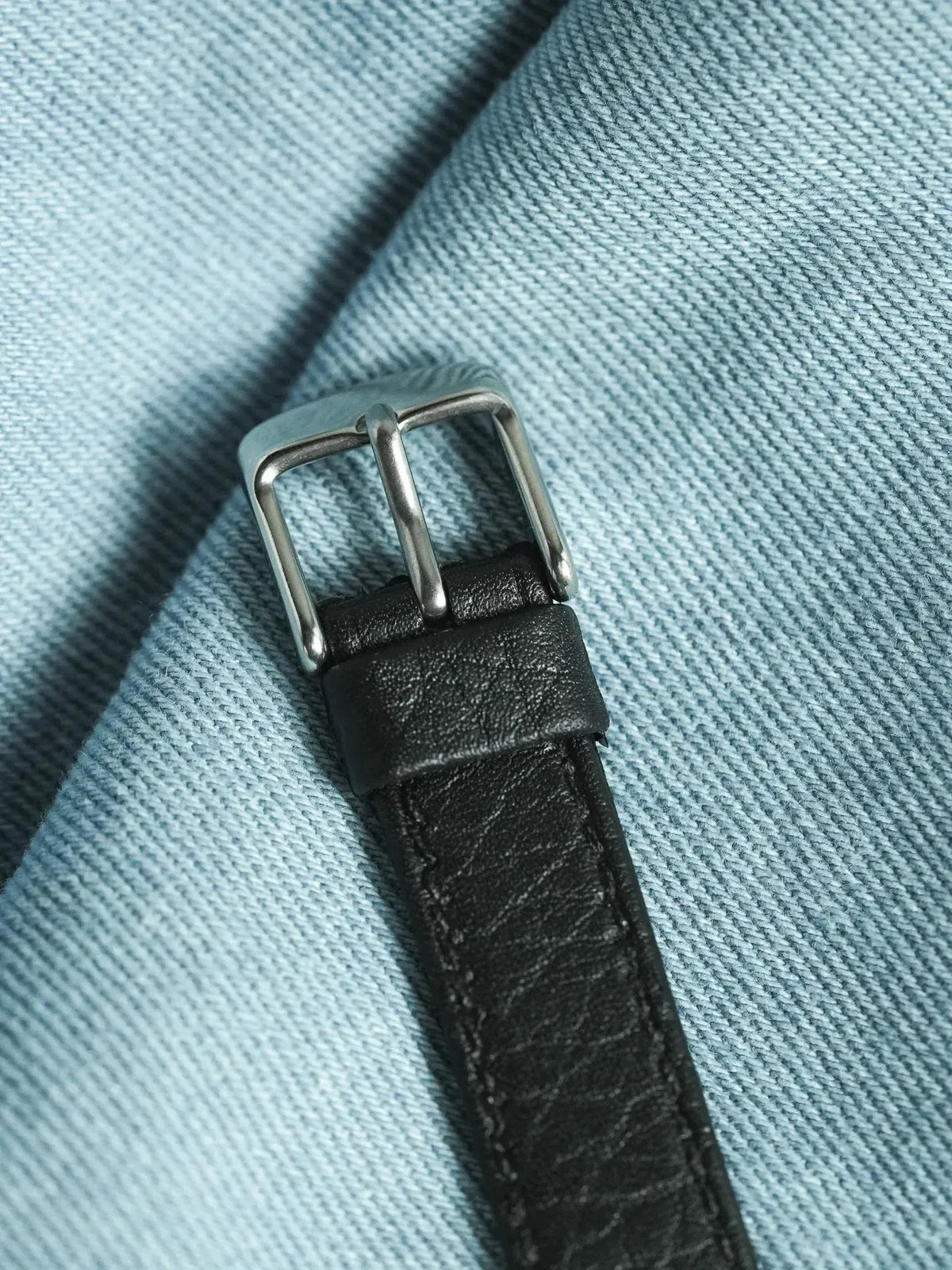 Black leather watch strap with silver buckle on light blue denim