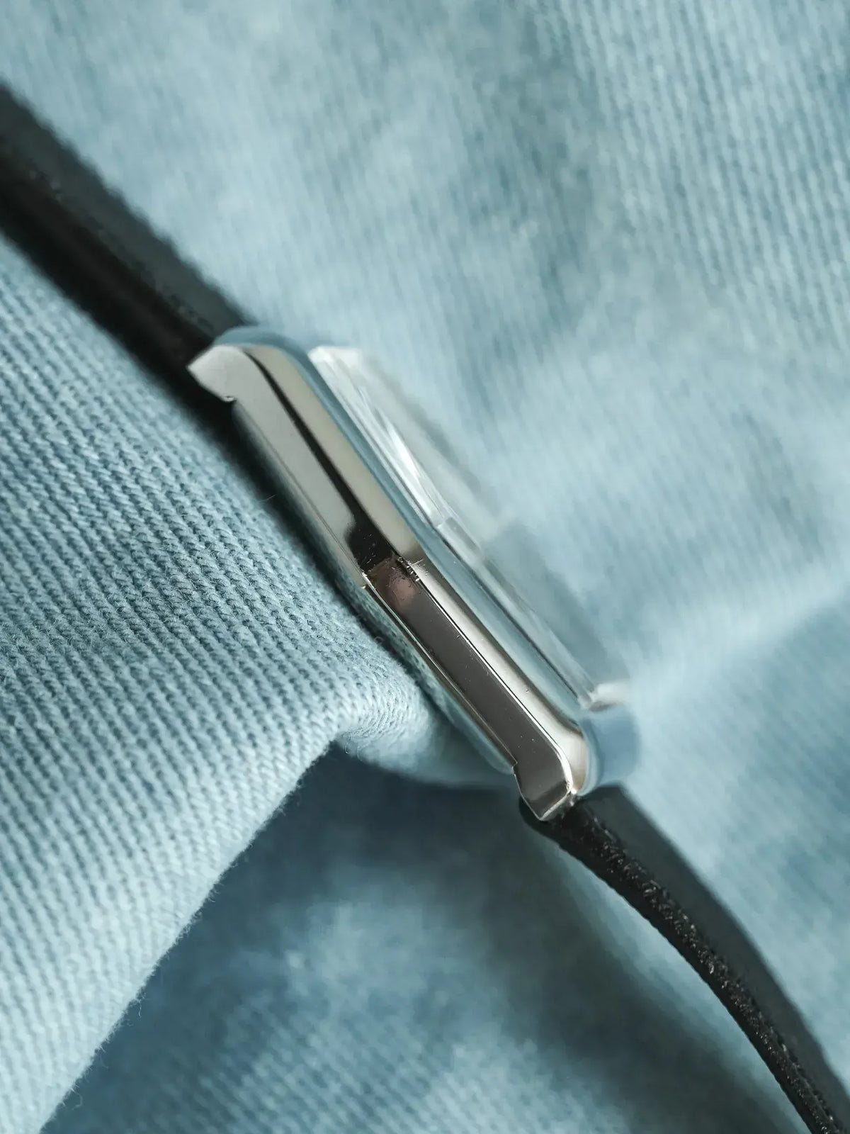Vintage Cartier Tank watch with steel case and black leather strap on blue fabric
