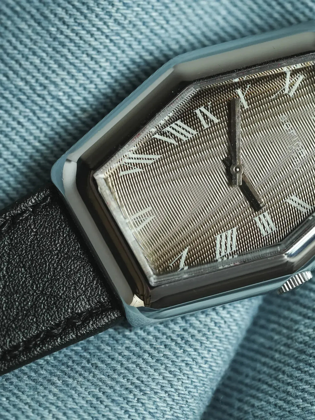 Universal Genève vintage watch with textured dial, Roman numerals, black leather strap on denim