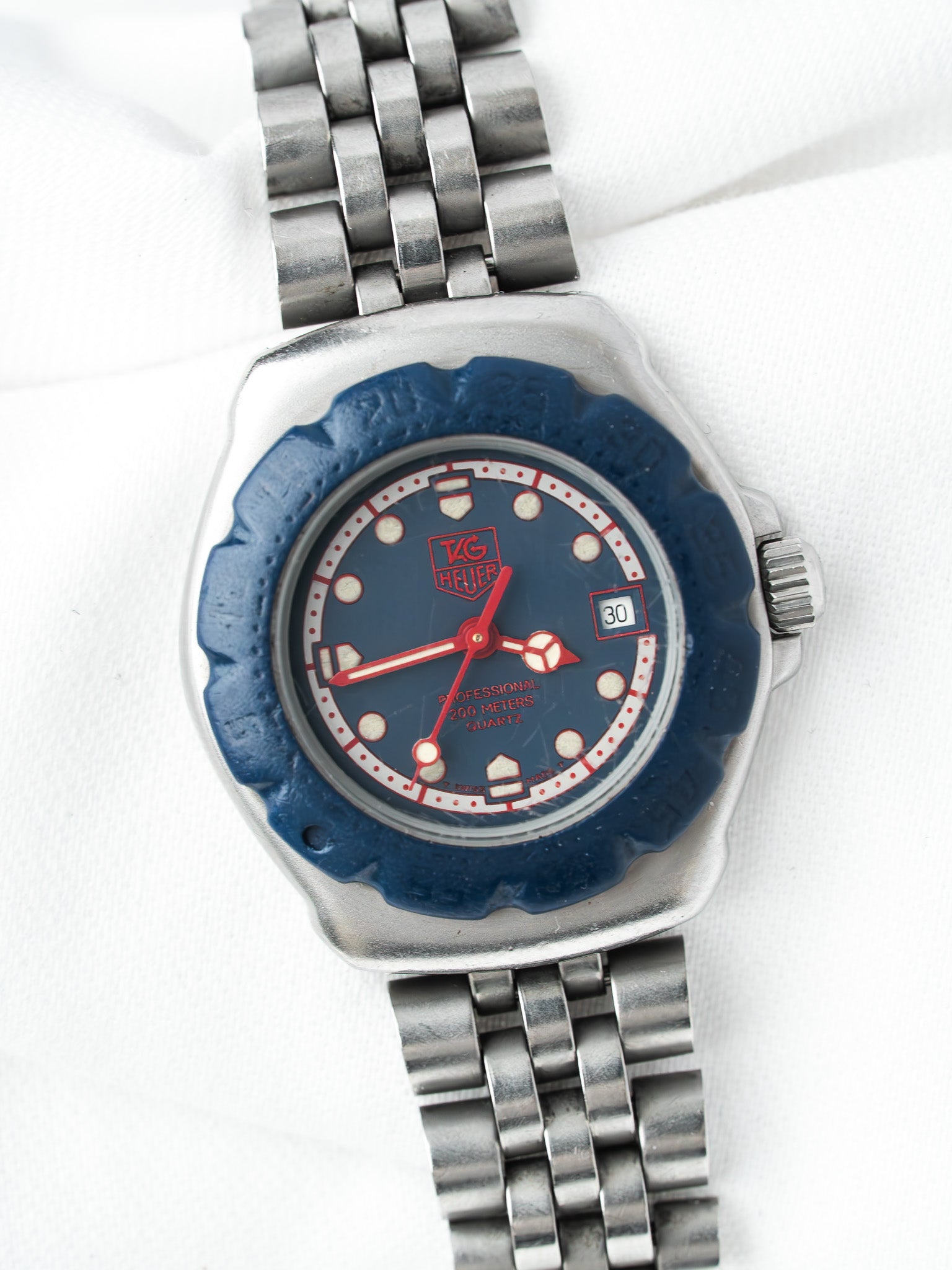TAG Heuer vintage watch with blue dial, red hands, steel bracelet on white background