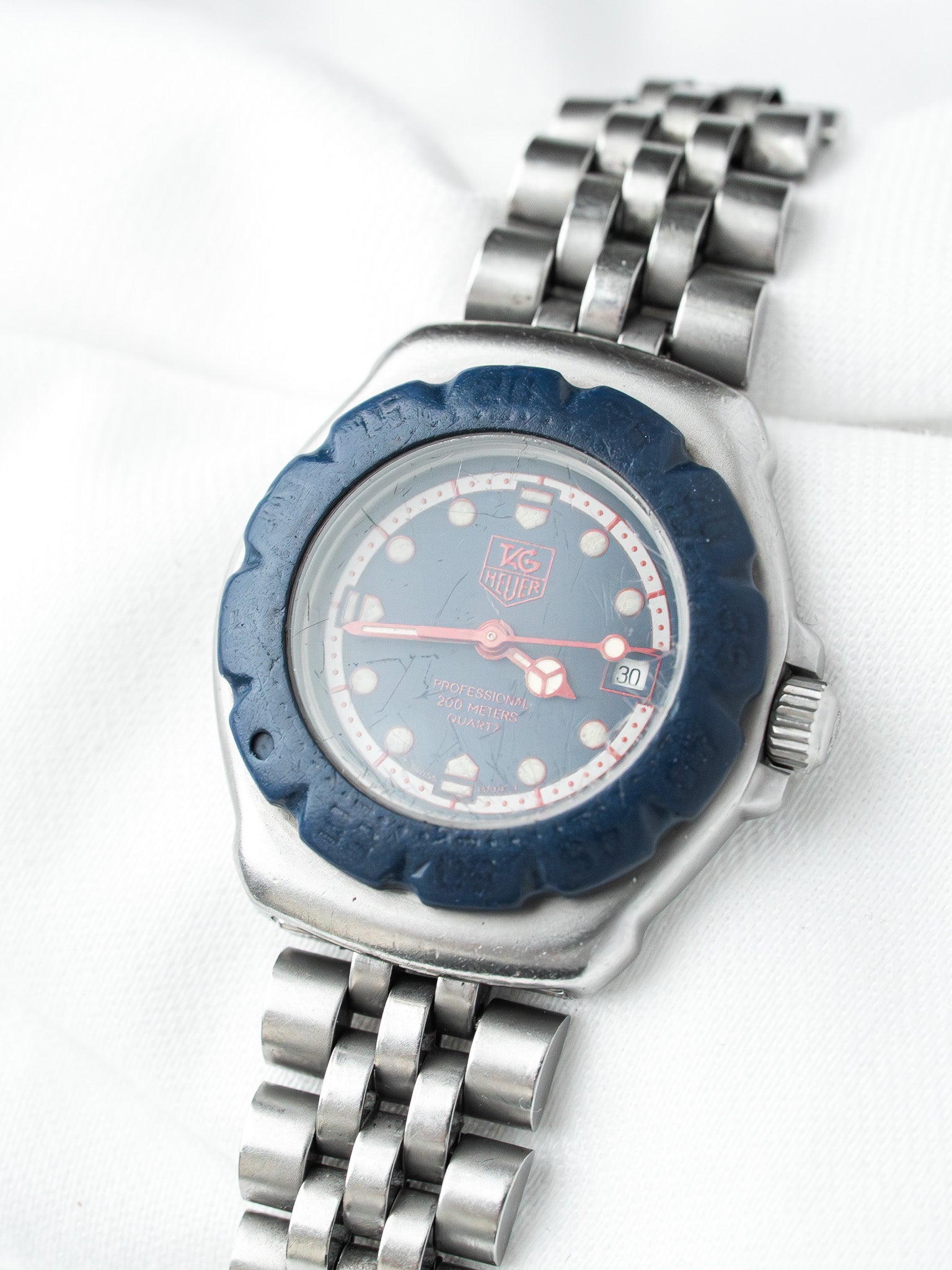 TAG Heuer Professional vintage watch with blue bezel, silver case, and steel bracelet on white background