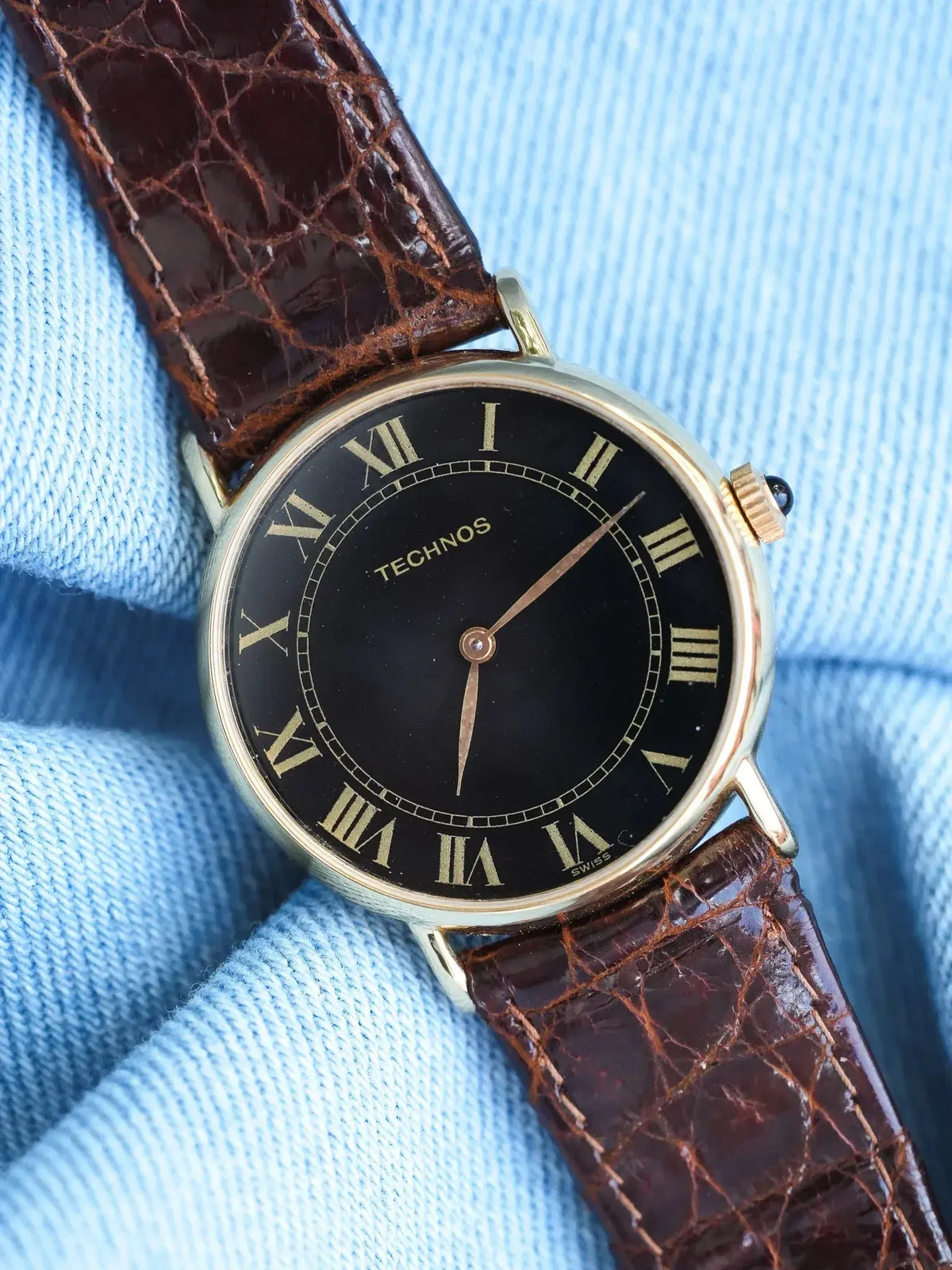 Technos vintage watch with black dial, gold Roman numerals, brown alligator strap on blue fabric