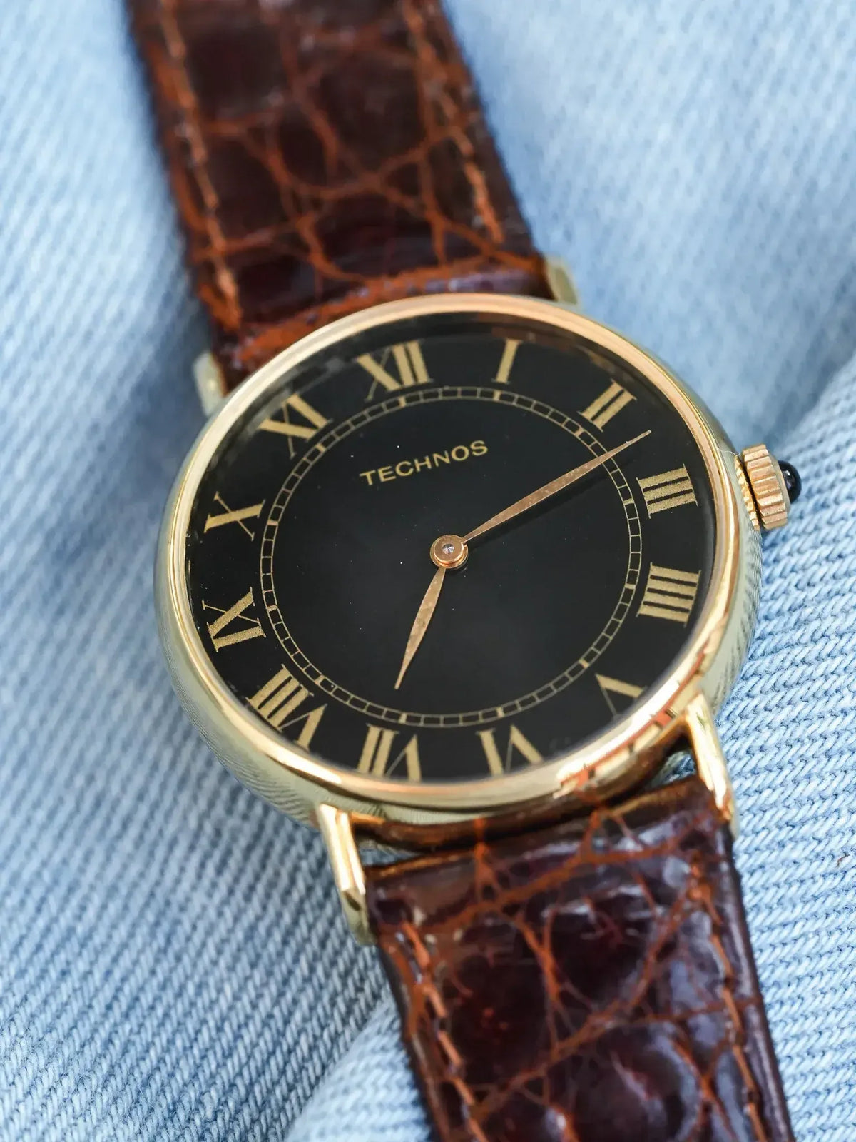 Technos vintage watch with gold case, black dial, Roman numerals, brown crocodile strap on denim