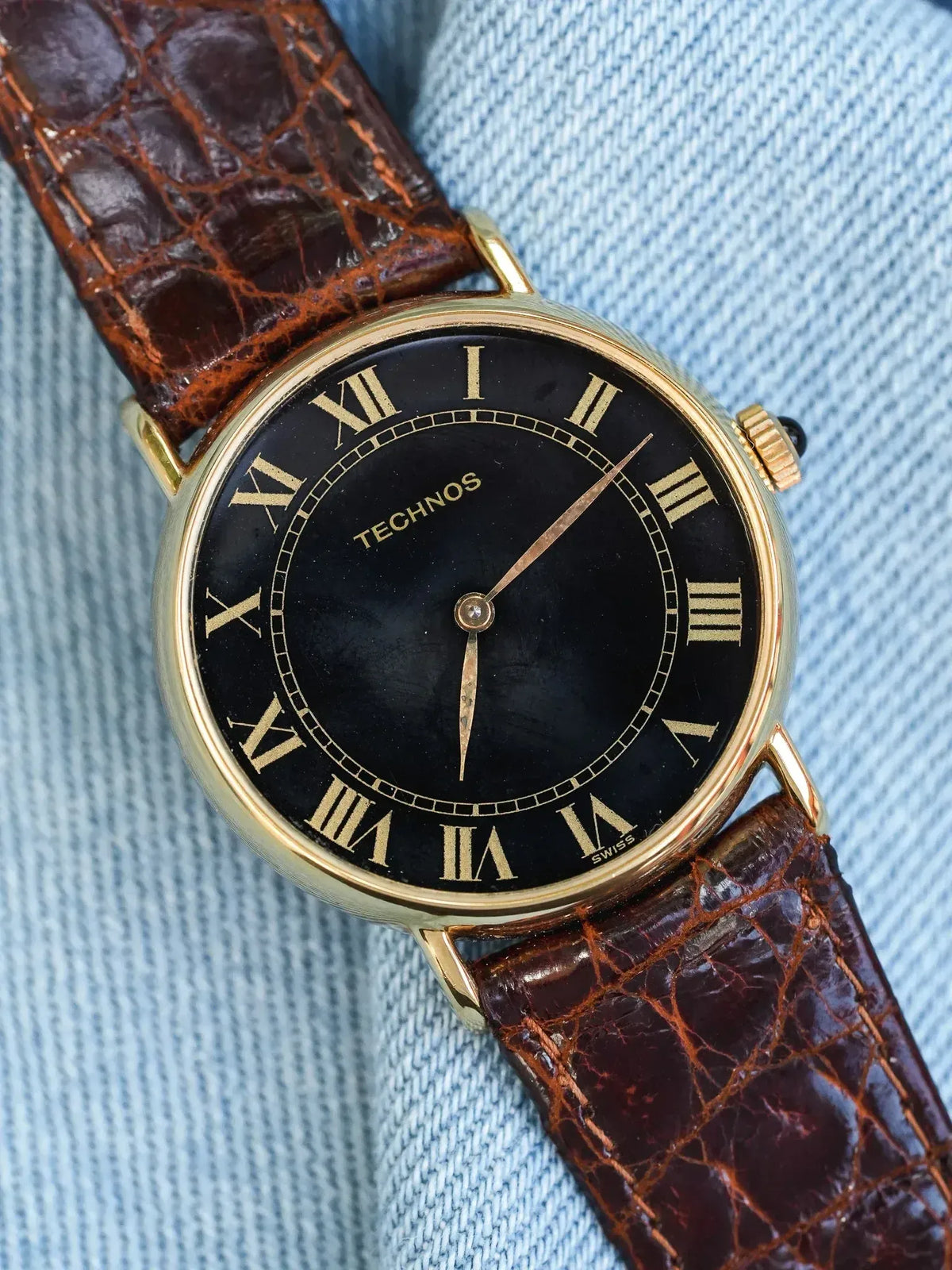 Technos vintage watch with gold case, black dial, Roman numerals, brown alligator strap on denim