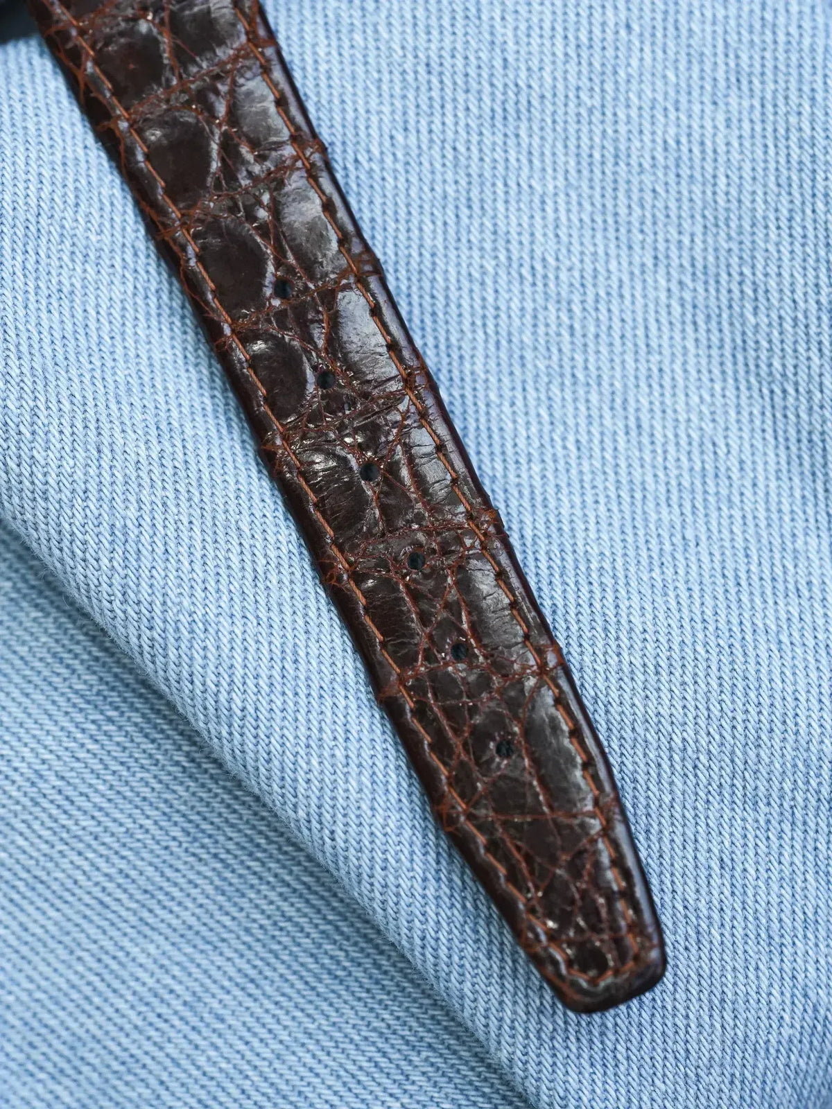 Brown alligator leather watch strap with orange stitching on blue fabric
