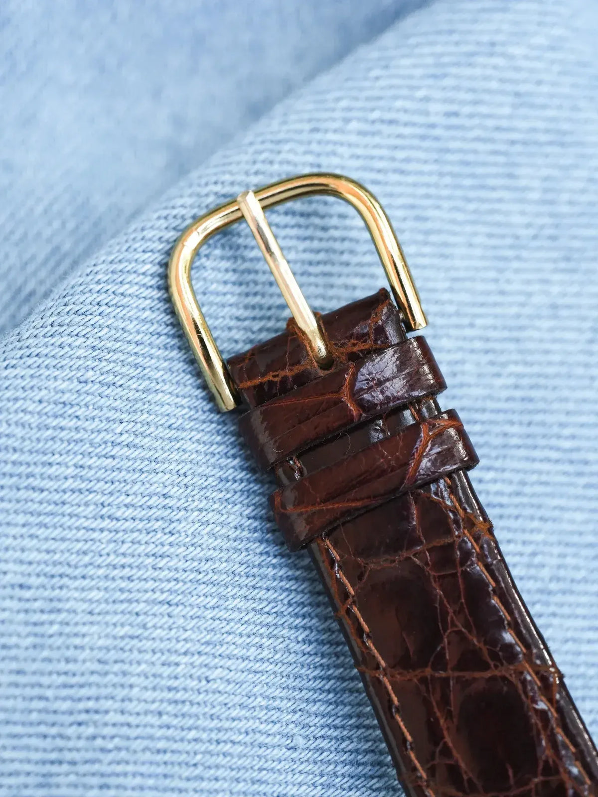 Brown alligator leather watch strap with gold buckle on denim background
