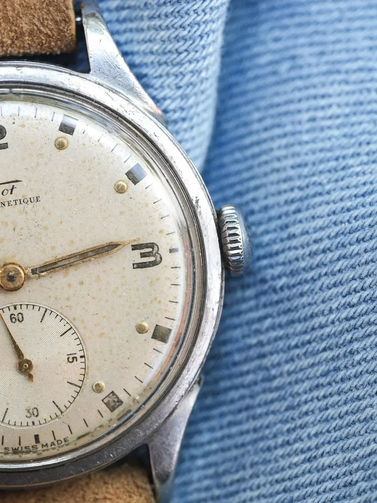 Vintage Doxa wristwatch with cream dial, steel case, and brown leather strap on denim