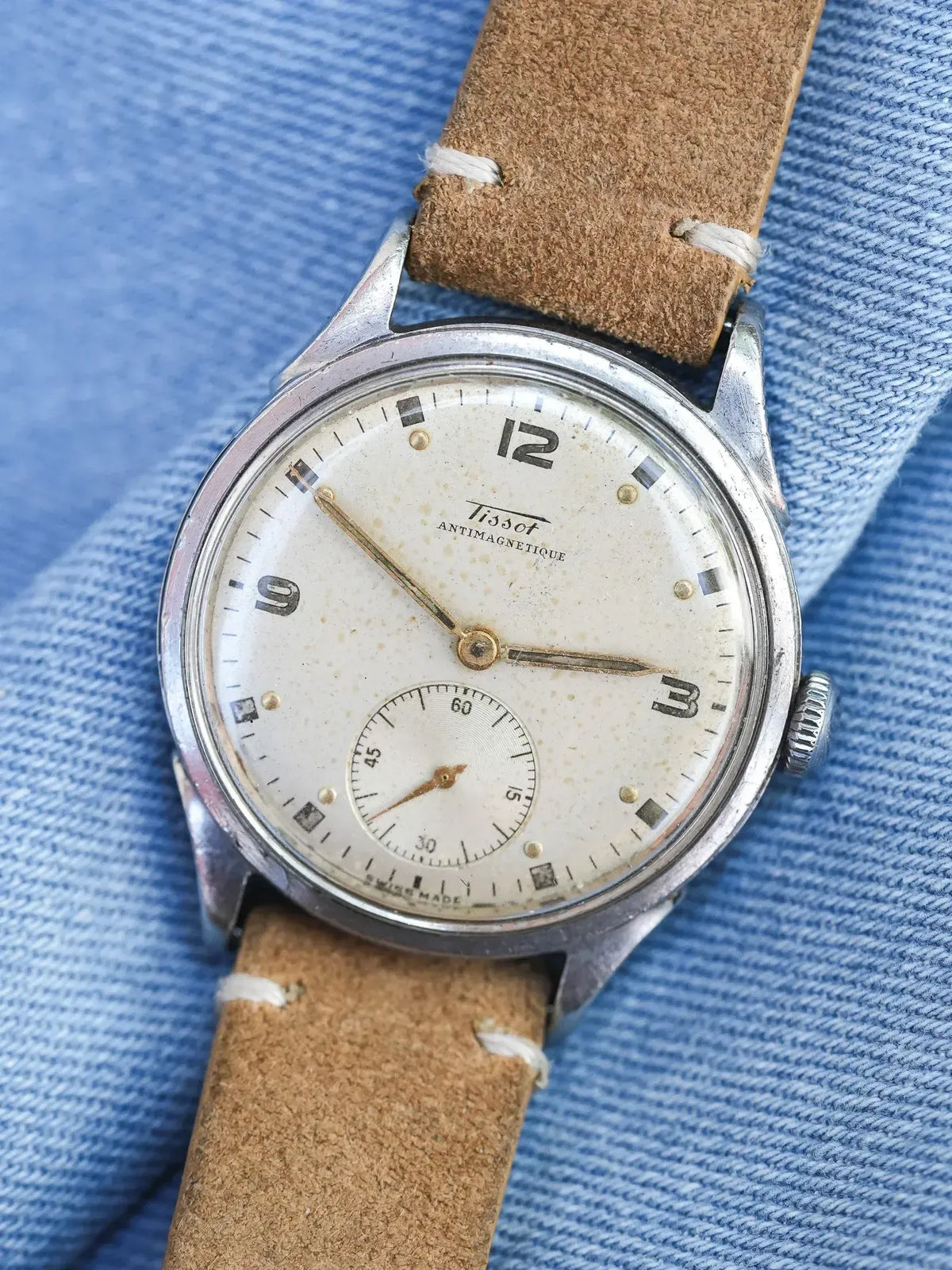 Vintage Tissot Antimagnetique watch with cream dial, steel case, brown leather strap on denim
