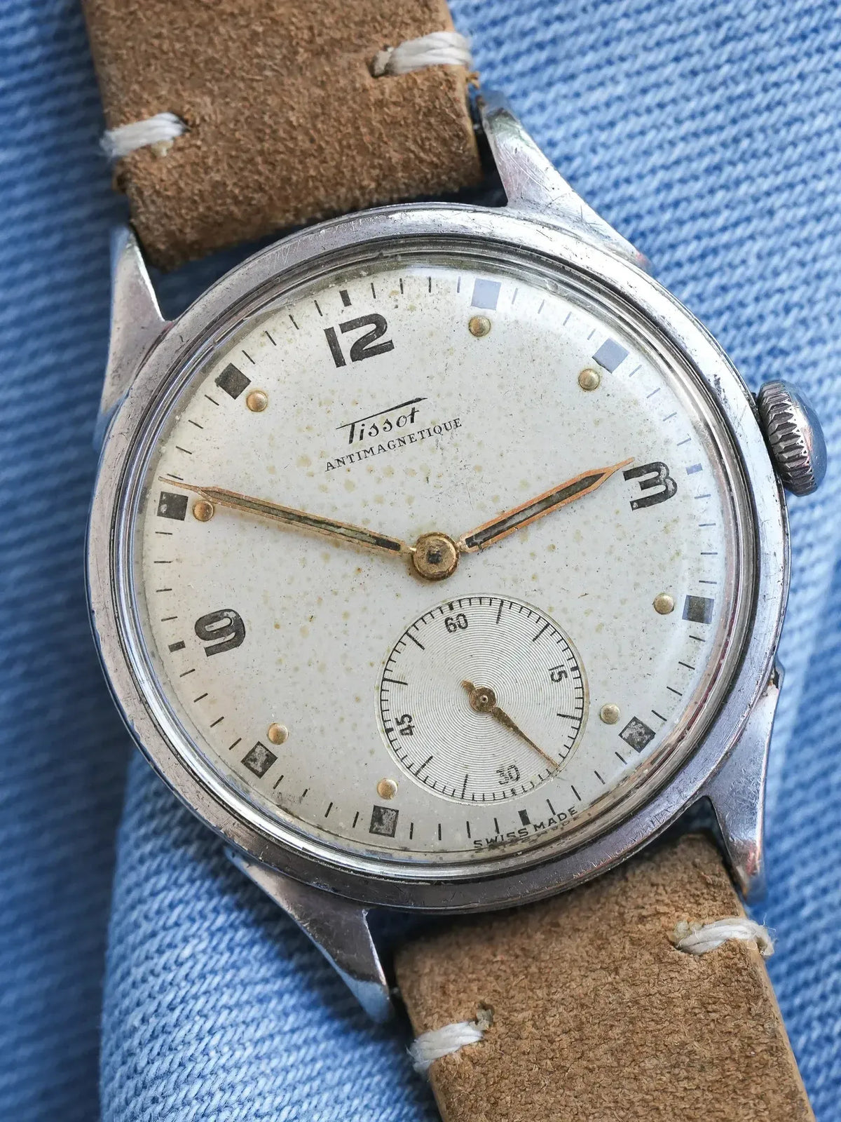 Vintage Tissot Antimagnetique watch with cream dial, steel case, brown leather strap on denim