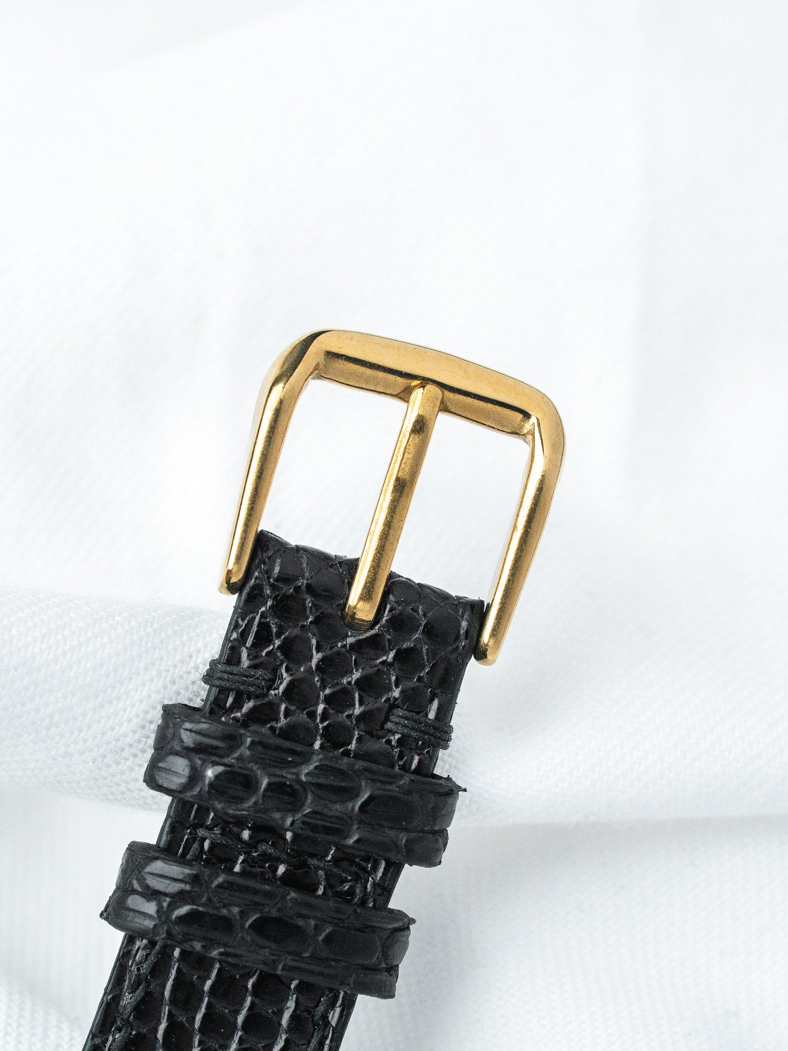 Black alligator leather watch strap with gold buckle on white background