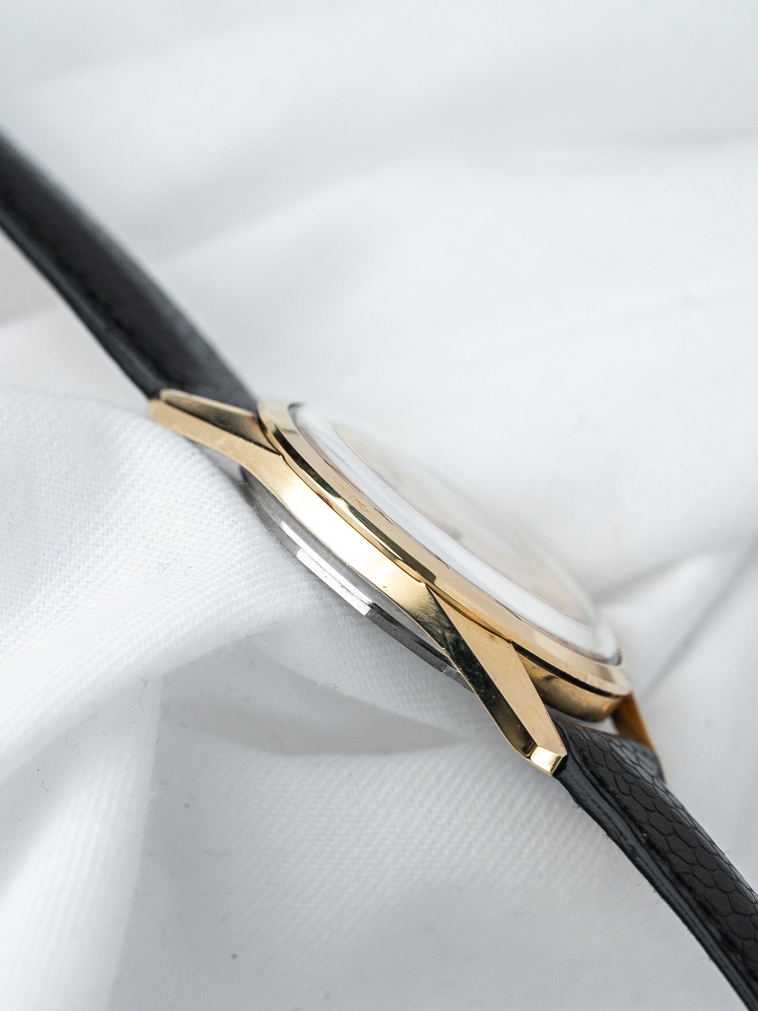 Vintage Rolex watch with gold case, black leather strap, white dial on fabric