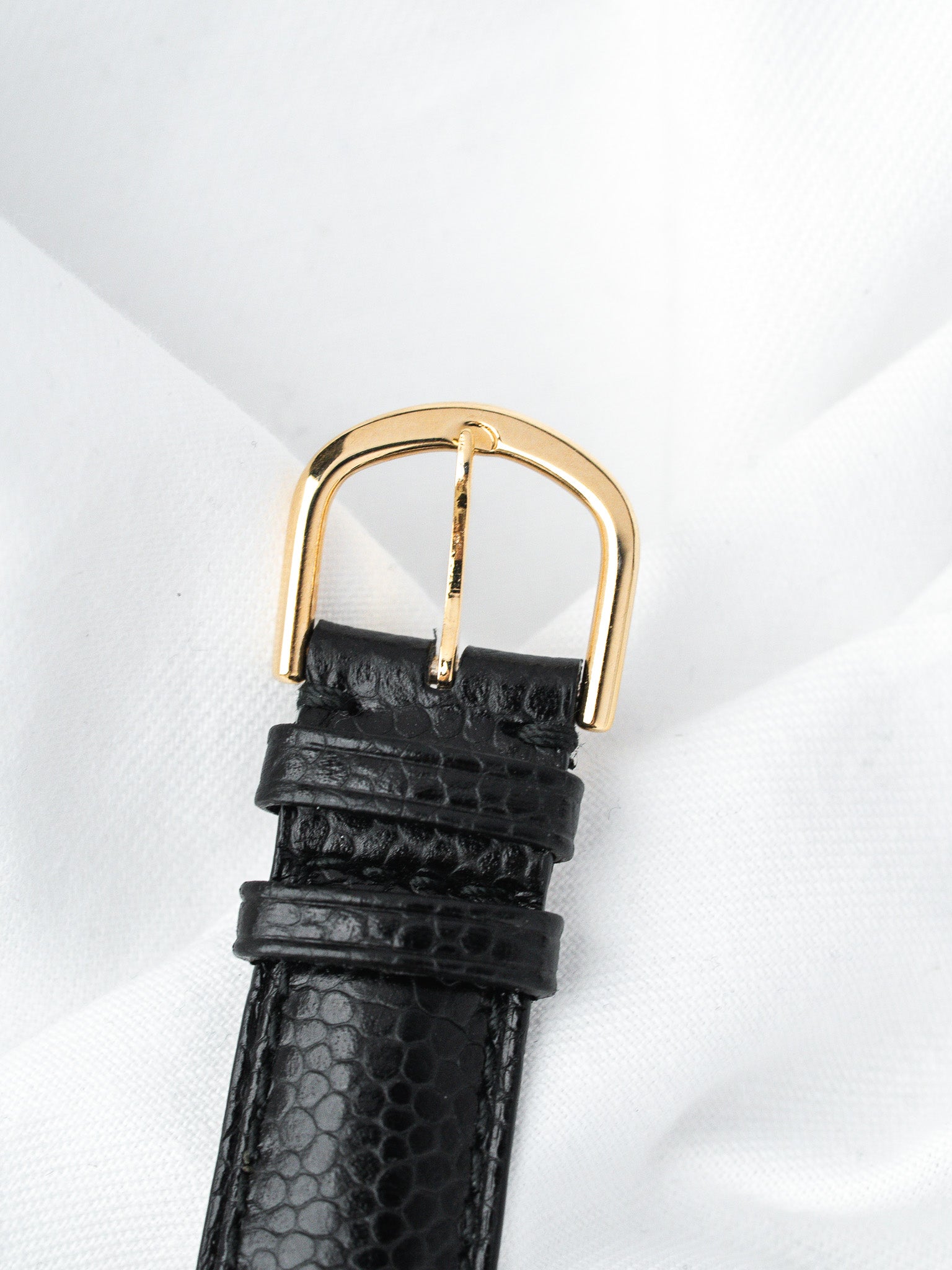 Black textured leather watch strap with gold buckle on white background