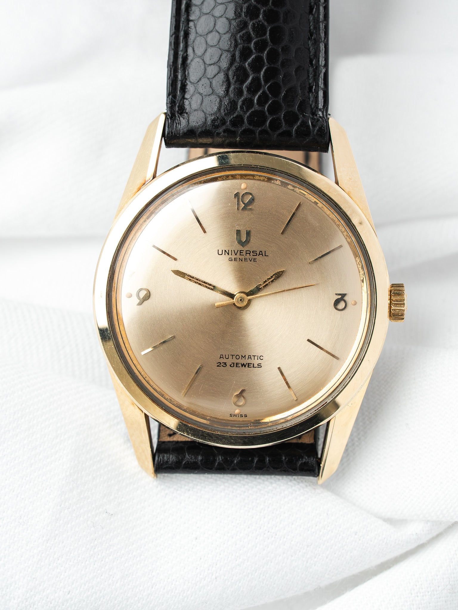 Universal Genève vintage watch with gold case, champagne dial, black lizard strap on white background