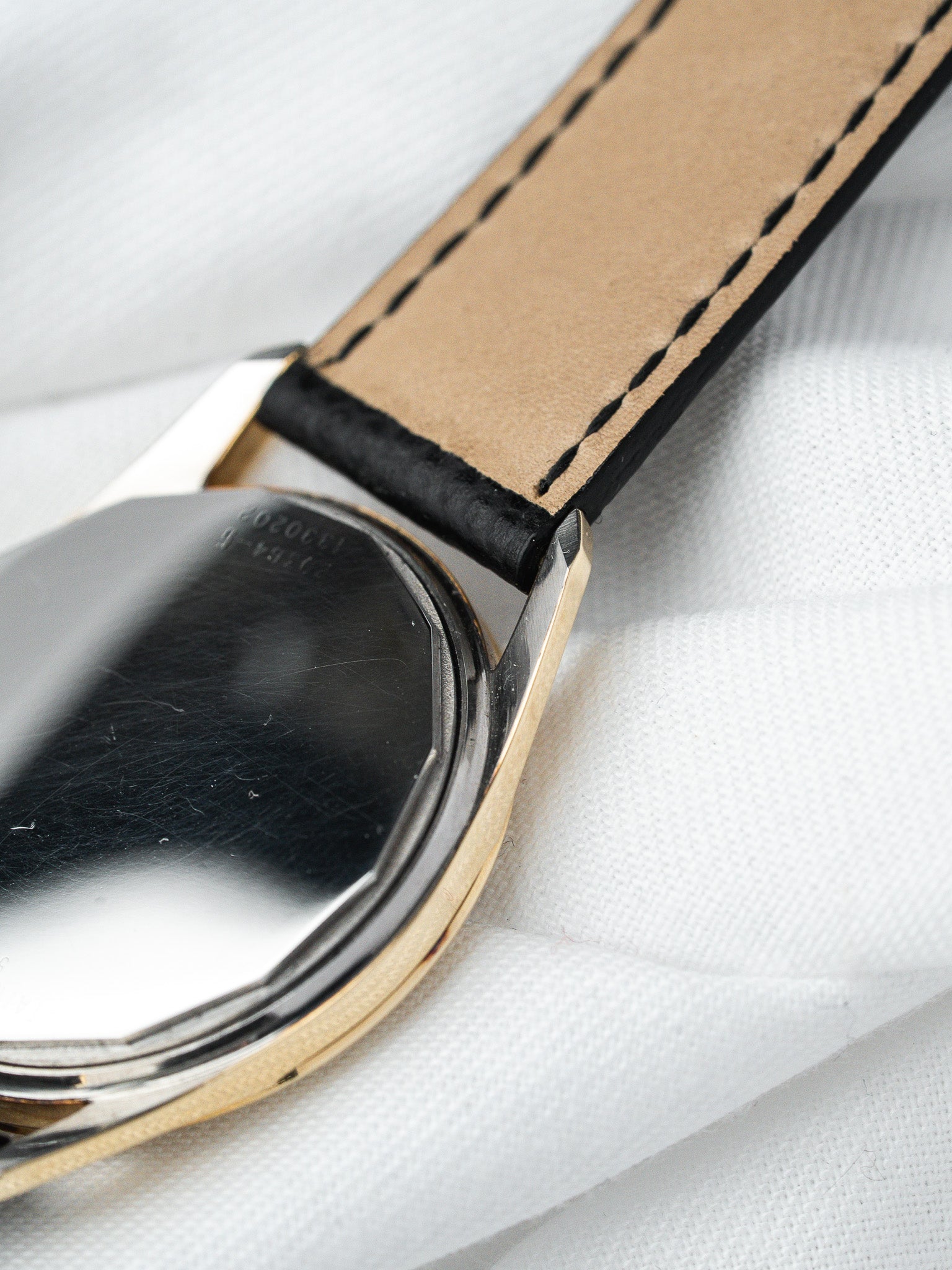 Vintage Omega watch with gold-toned case and black leather strap on white fabric