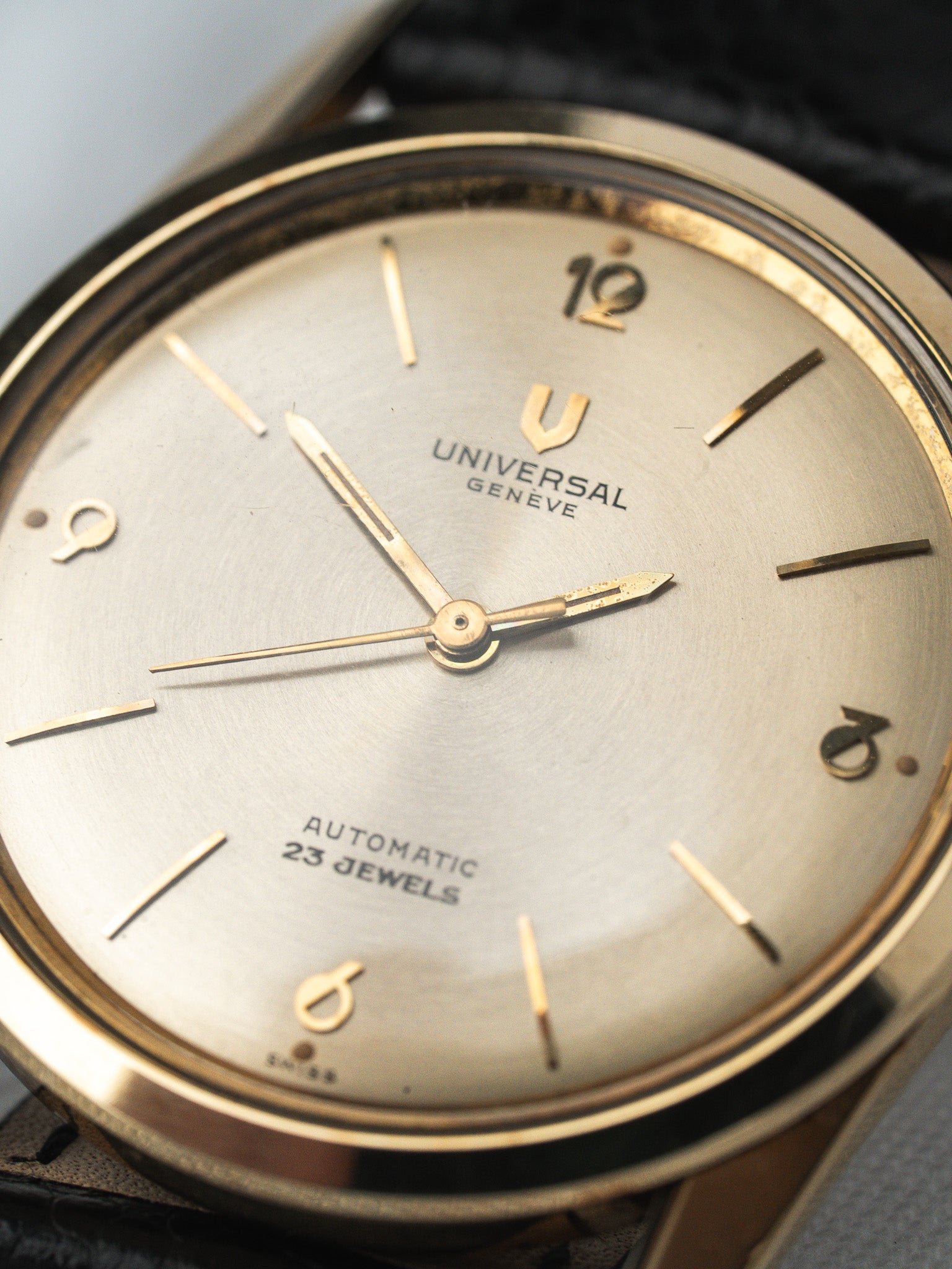 Universal Genève vintage automatic watch with silver dial, gold hands, and black leather strap
