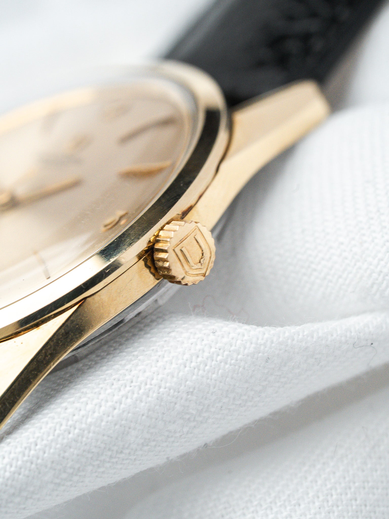 Vintage Universal Genève watch with gold case, black leather strap, on white fabric