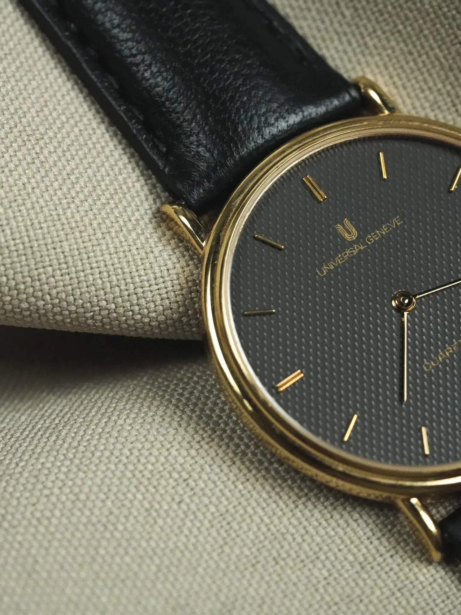 Universal Genève vintage watch with gold case, black textured dial, and black leather strap