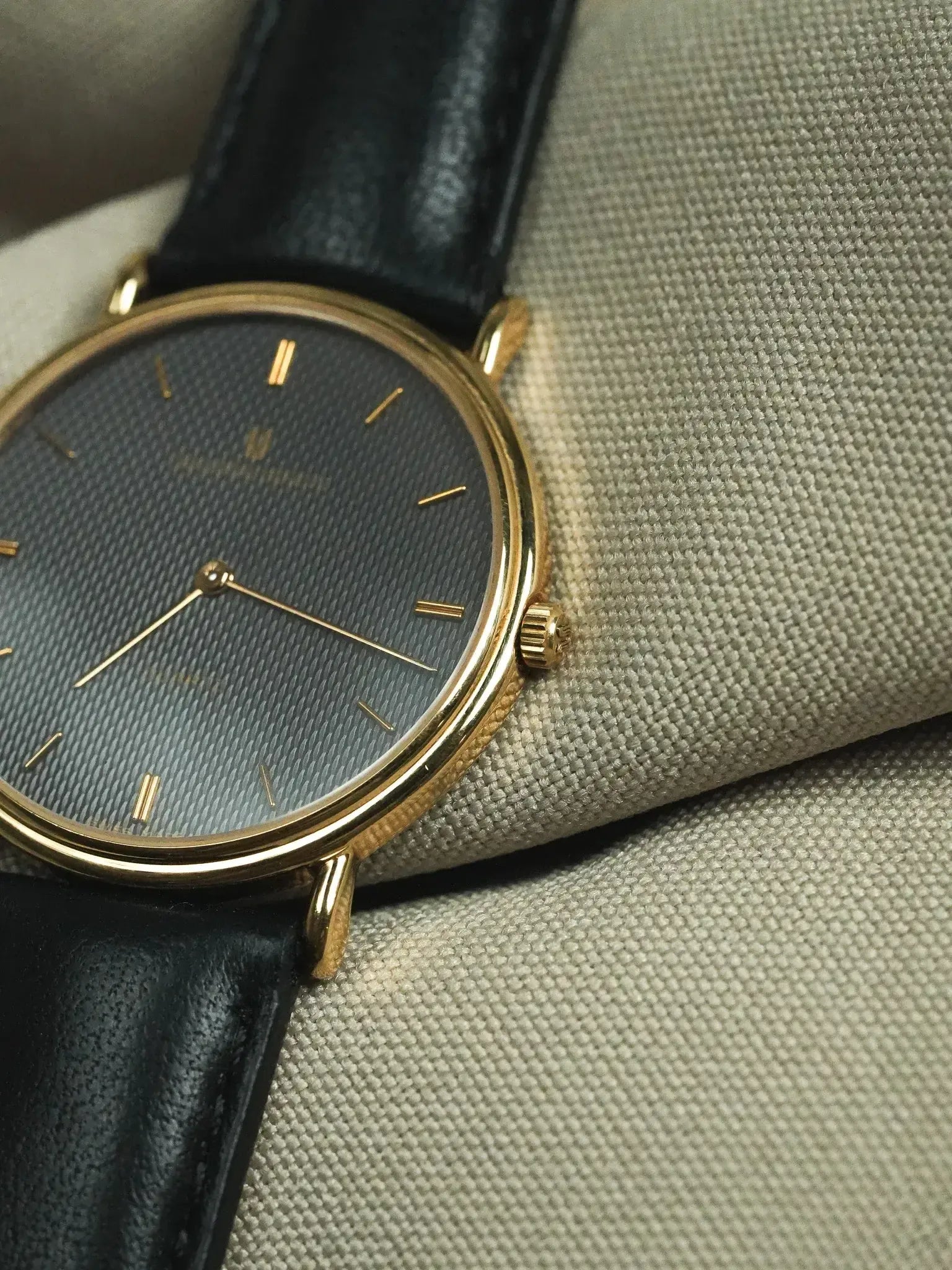 Universal Genève vintage watch with gold case, grey textured dial, black leather strap on fabric
