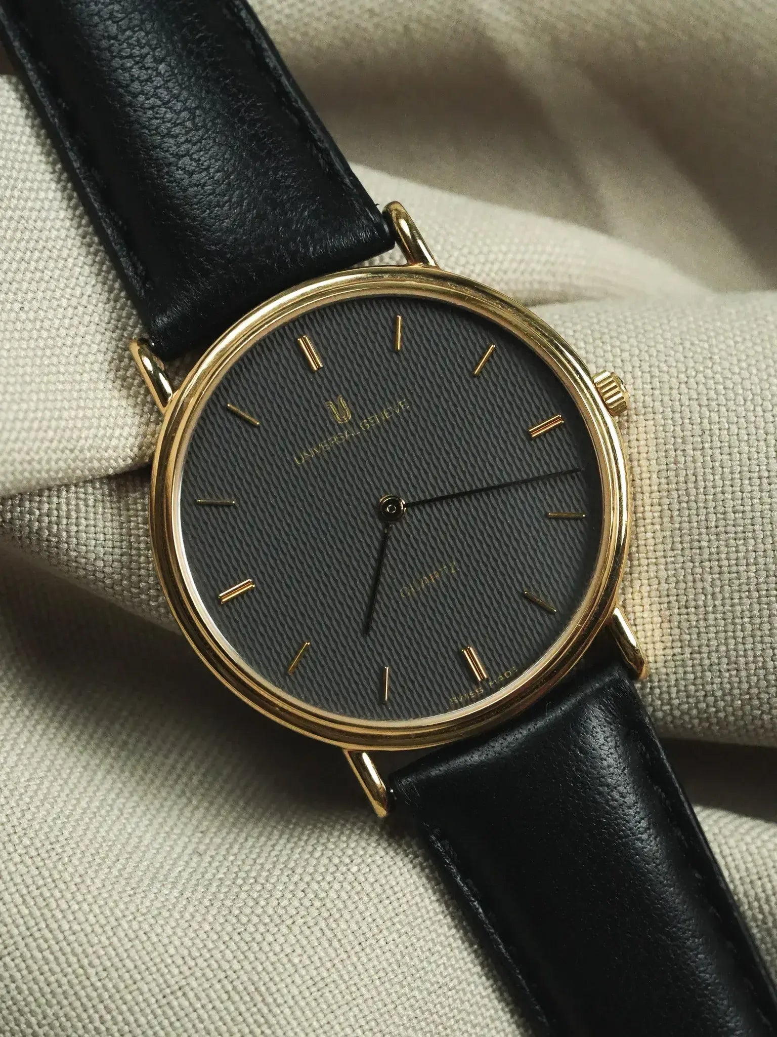 Universal Genève vintage watch with gold case, black textured dial, and black leather strap