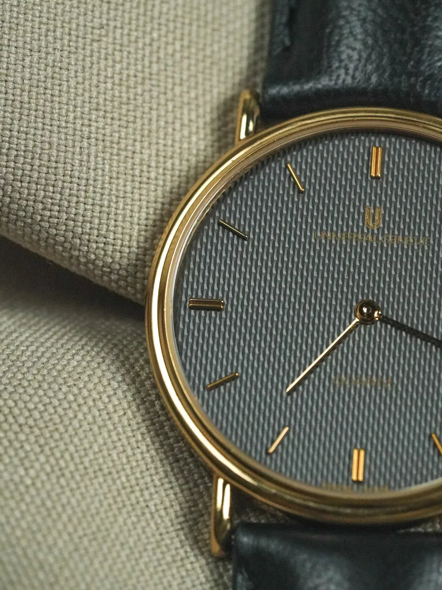 Universal Genève vintage watch with gold case, textured grey dial, and black leather strap