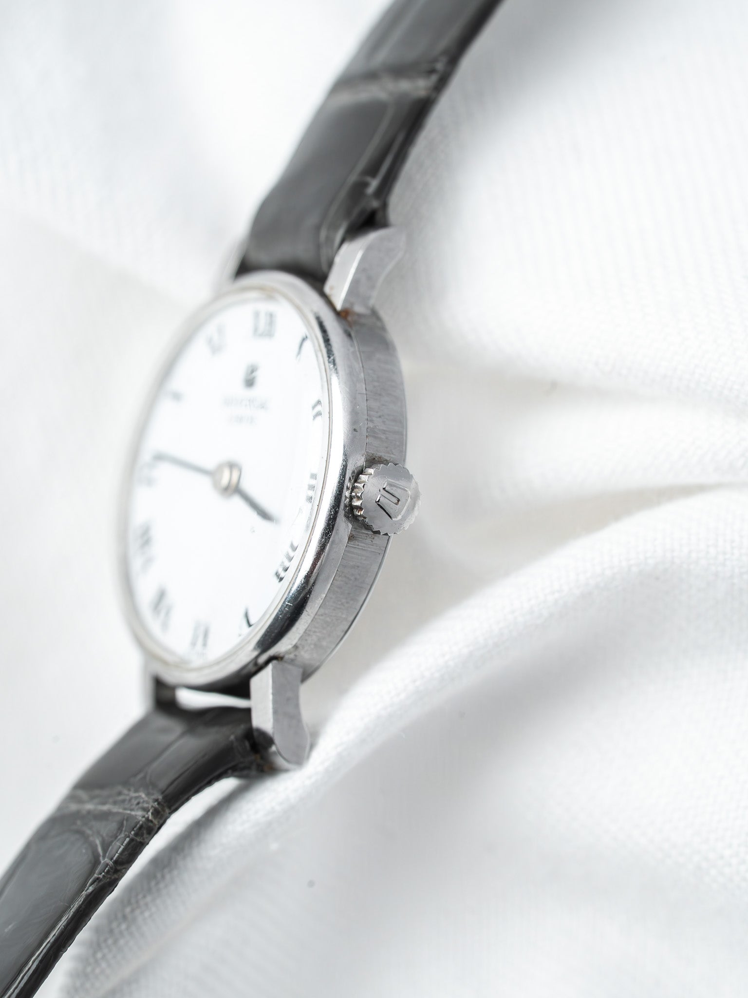 Vintage Universal Genève watch with white dial, black leather strap, silver case on white fabric