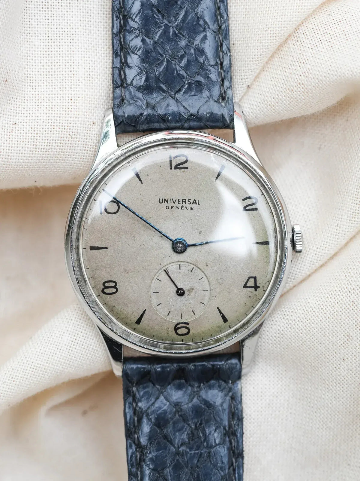 Universal Geneve vintage watch with silver dial, blue leather strap, on fabric background