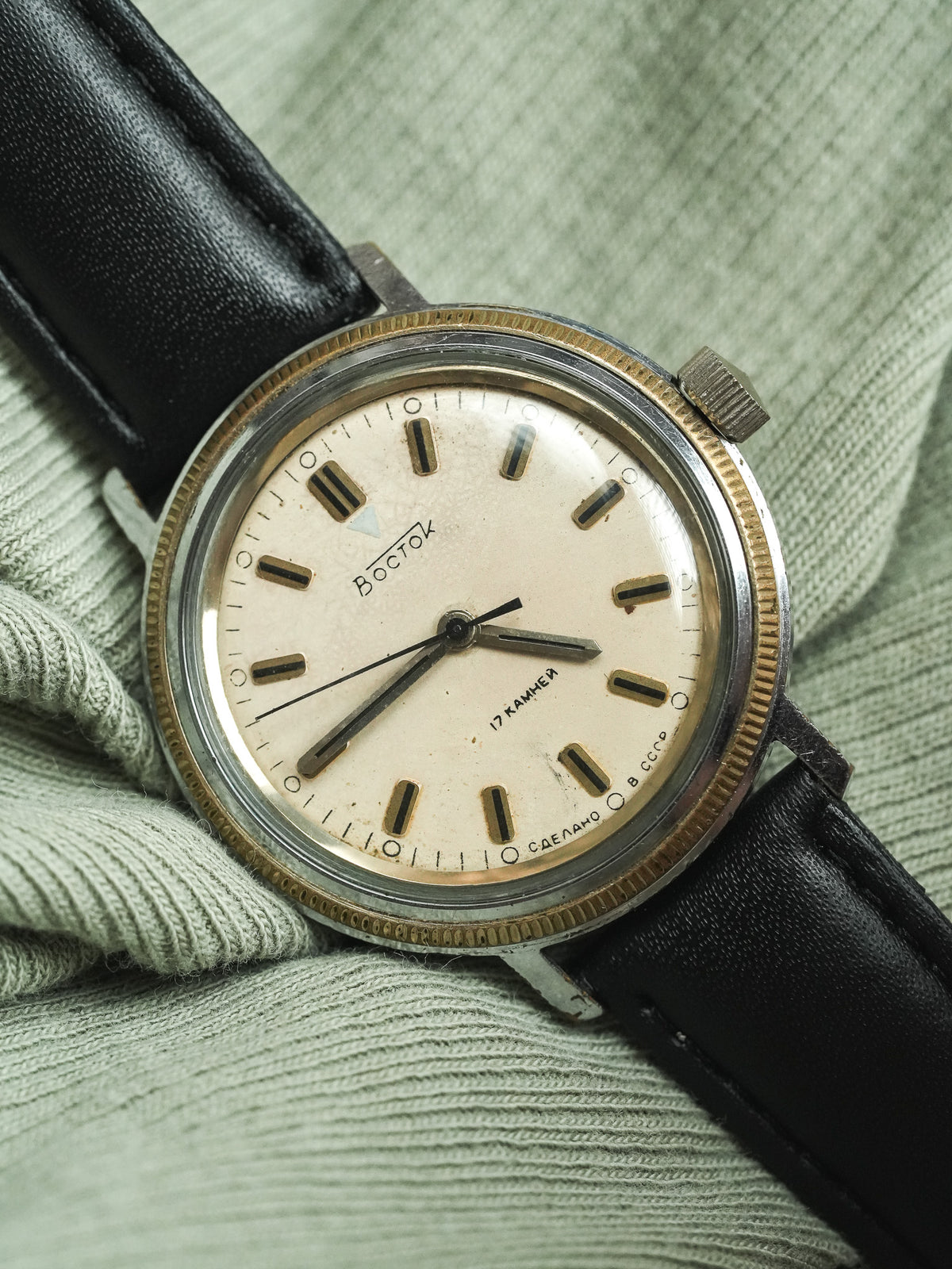 Vintage Vostok watch with cream dial, black leather strap, resting on green fabric