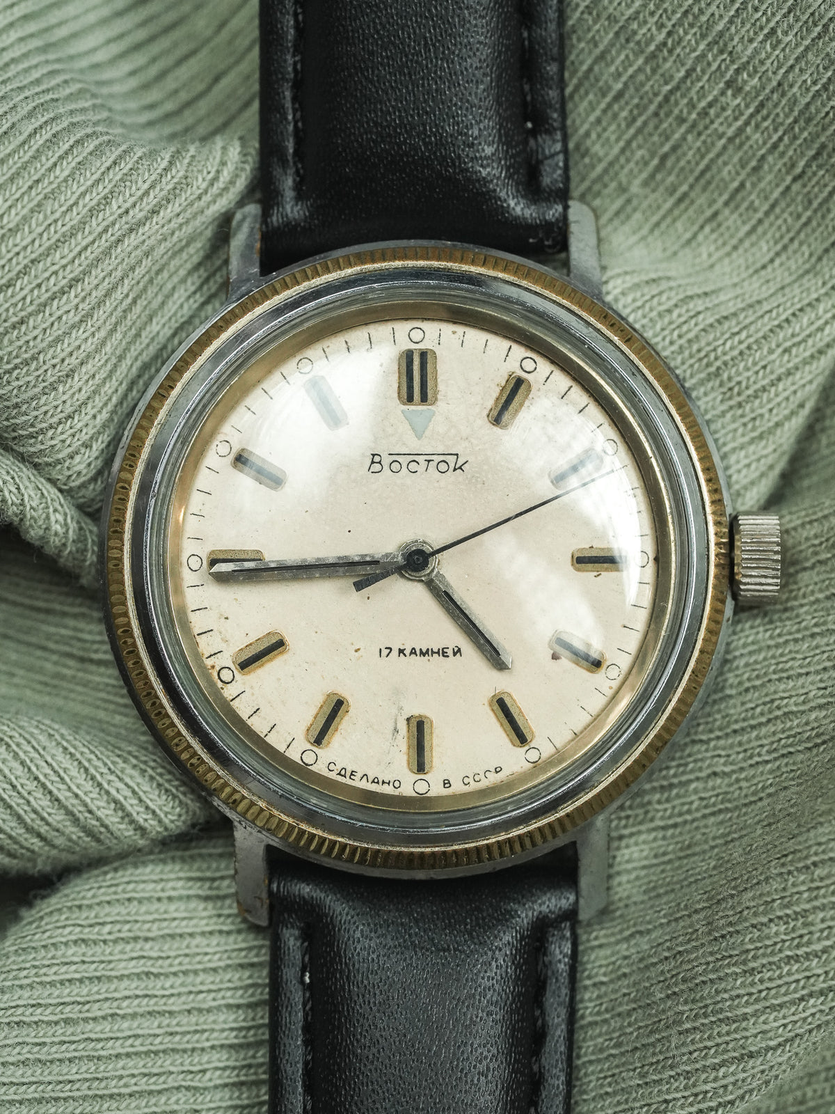 Vintage Vostok watch with cream dial, black leather strap, worn on green fabric