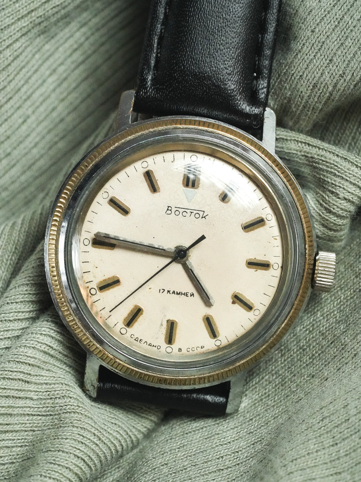 Vintage Vostok watch with cream dial, black leather strap, resting on green fabric