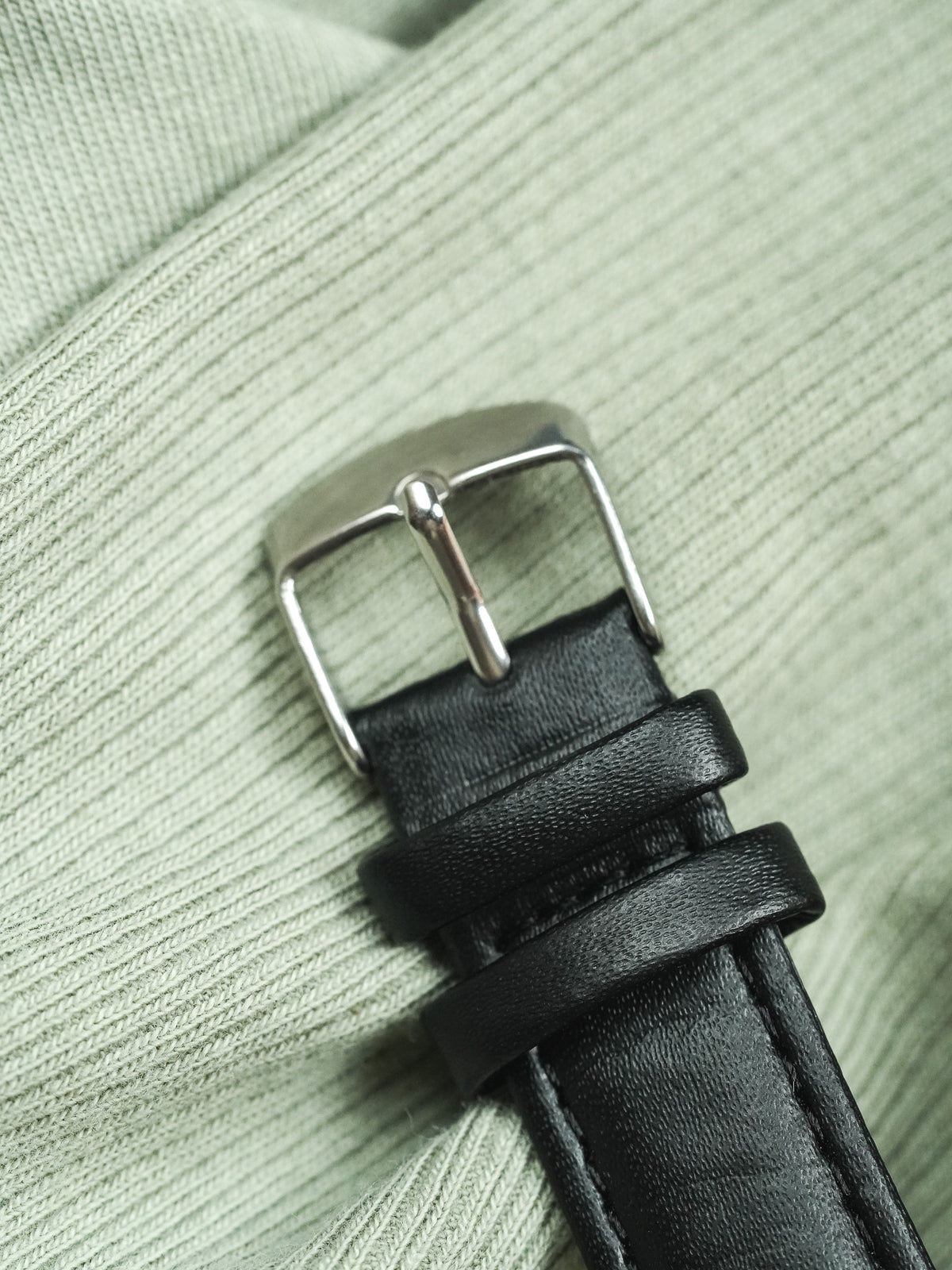 Black leather watch strap with silver buckle on textured green fabric