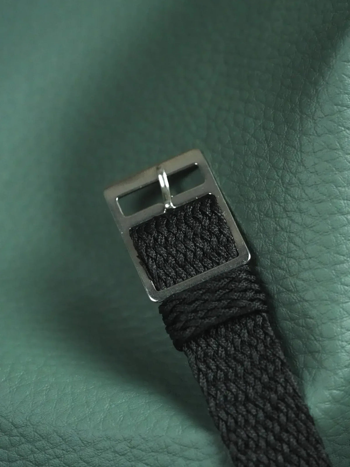 Black braided nylon watch strap with silver buckle on green leather
