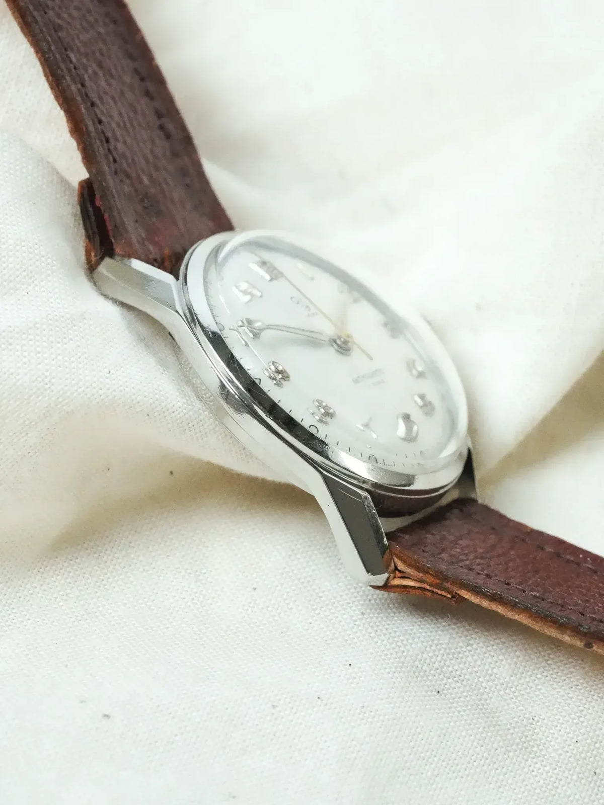 Vintage Universal Genève watch with silver case, white dial, and brown leather strap
